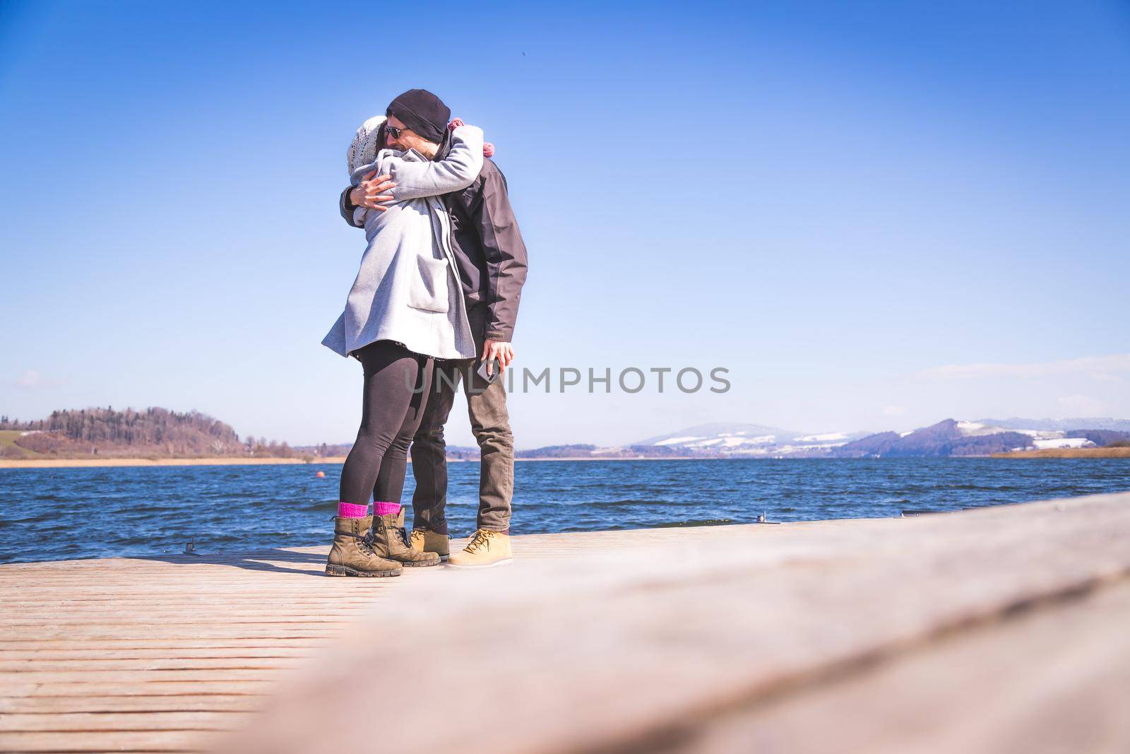 Young couple is standing on a footbridge and enjoys the view over the lake, winter time
