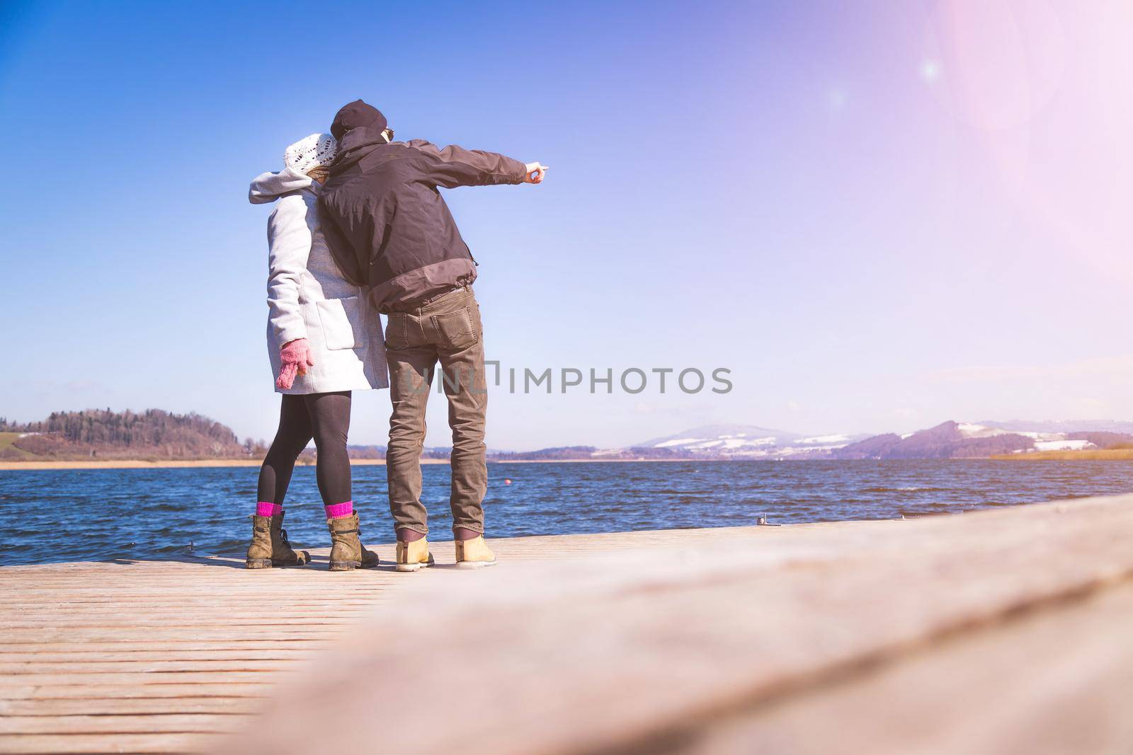 Young couple is standing on a footbridge and enjoys the view over the lake, winter time