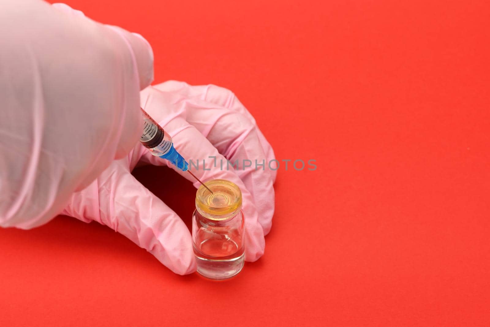 A medical worker wearing gloves holds a disposable syringe and a vial of a drug or vaccine. by Olga26