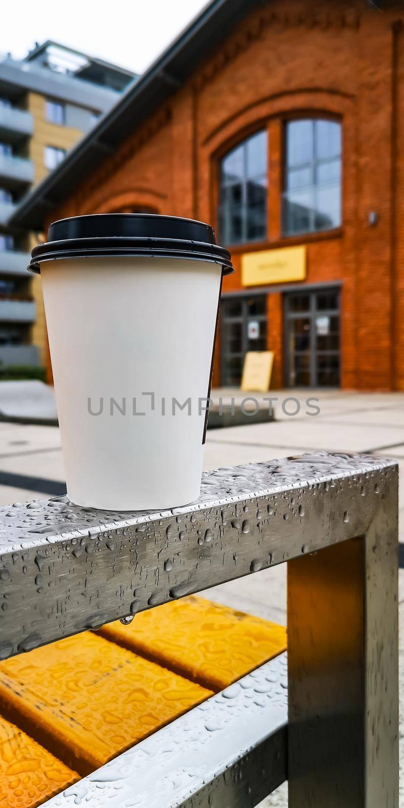 Coffee paper cup on wet railing of bench at rainy day