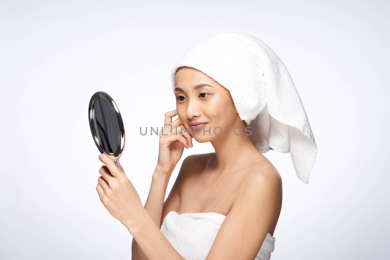 pretty woman with a towel on her head looks in the mirror skin care after shower. High quality photo