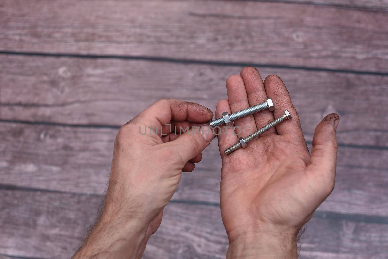 Bolts with nuts in their hands. Working men's hands are dirty from work. Close-up. On a wooden background.