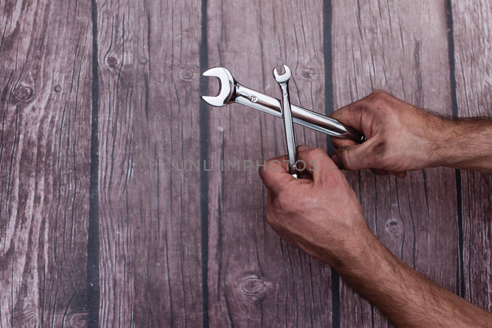 Chrome-plated wrenches in a man's work-smeared hands. On a wooden background. Close-up. copy space