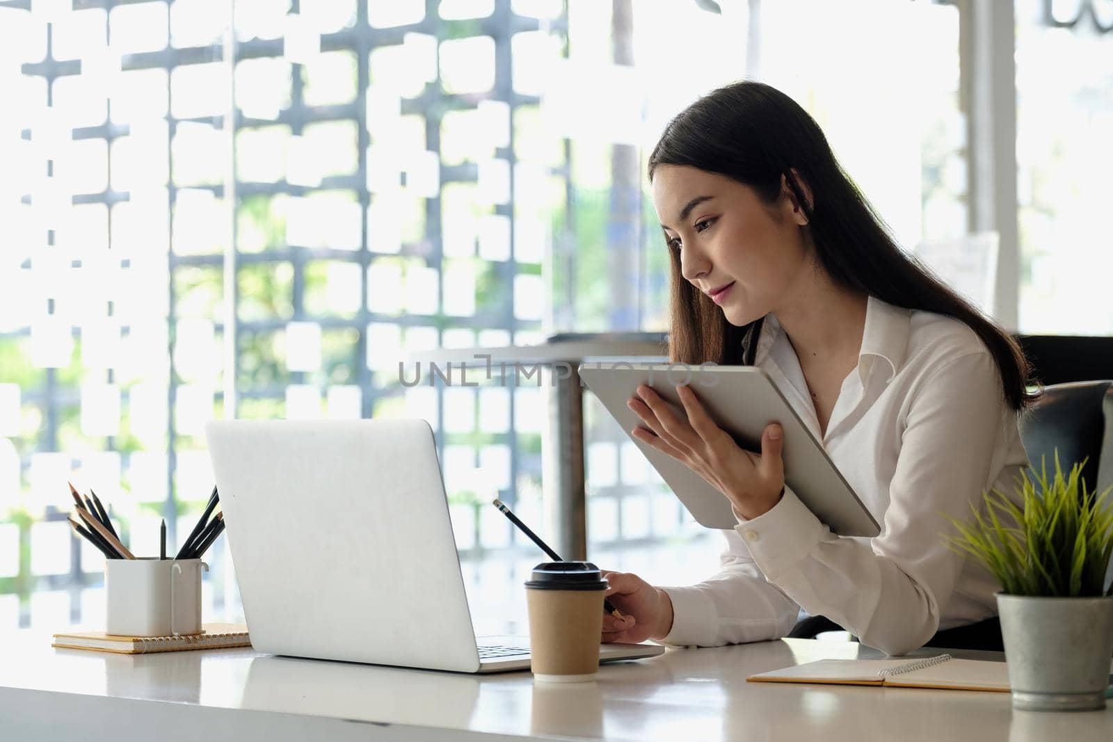 Beautiful business woman uses tablet and laptop while working in the office