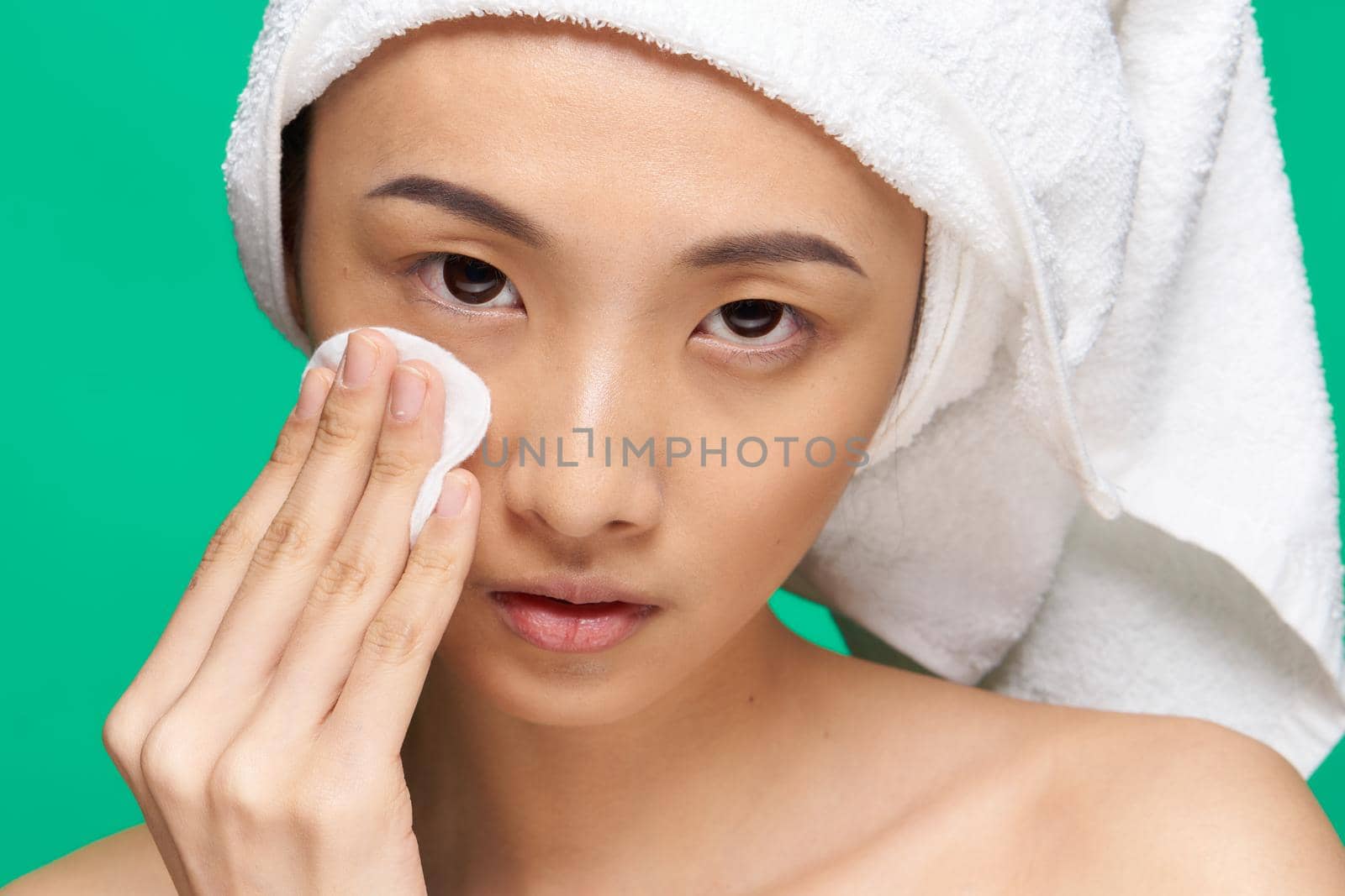 woman wipes her face with a cotton pad naked shoulders clean skin Green background. High quality photo