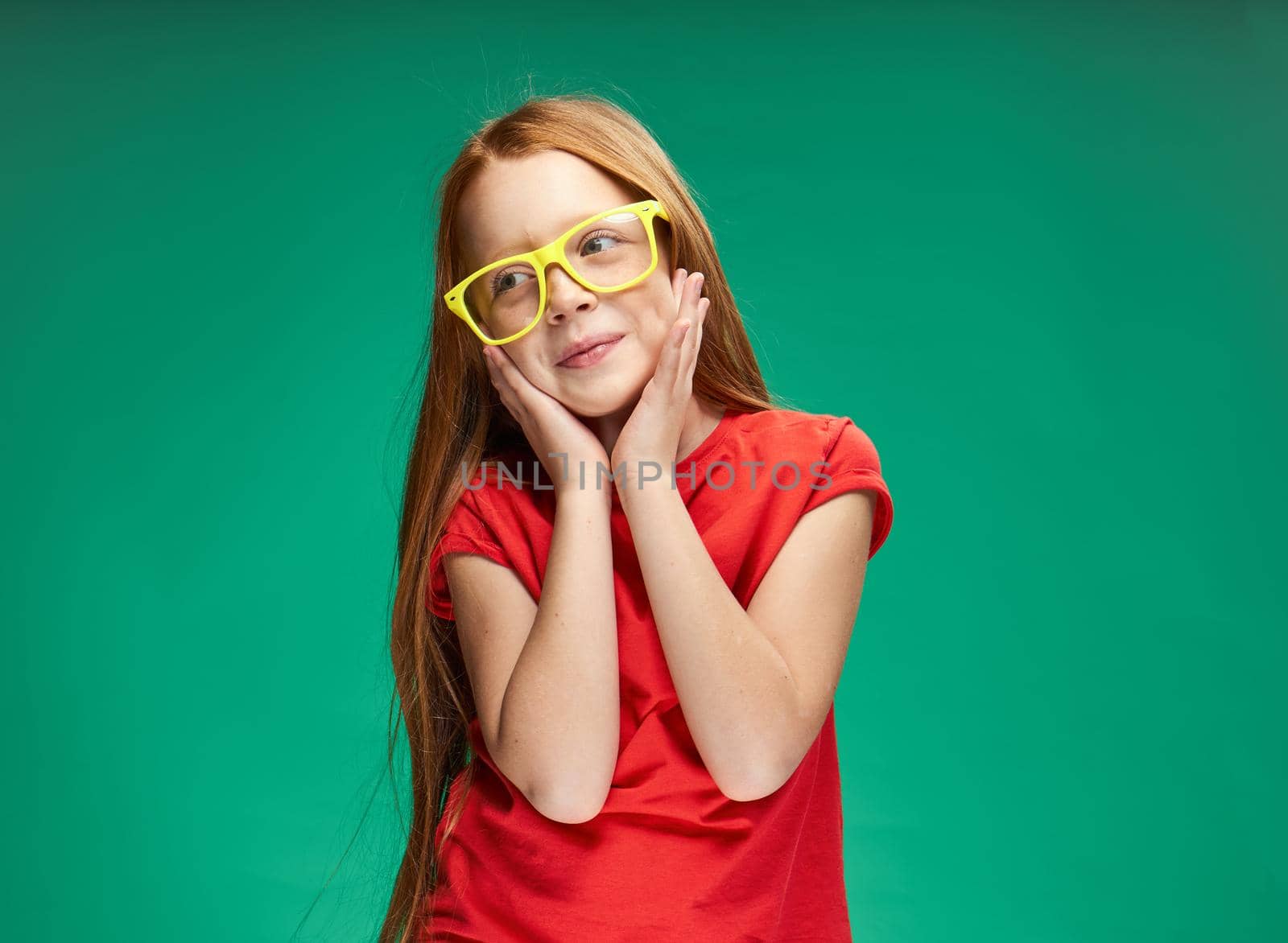 cute red-haired girl gesturing with her hands childhood green background school. High quality photo