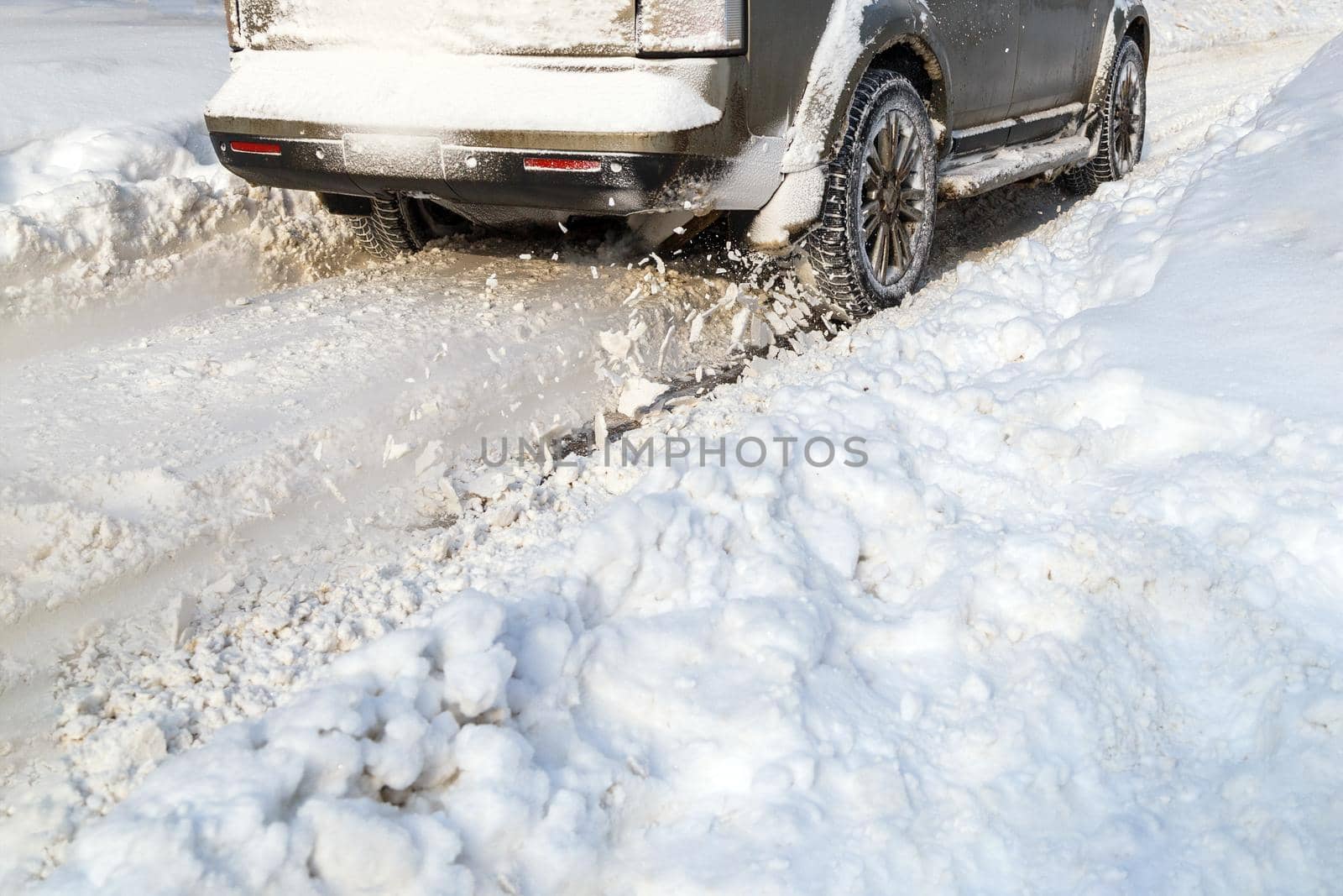 Road snow flies up from a vehicle's spinning wheel. Car's wheels spin and spew up pieces of snow it attempts to gain traction on the slippery road at winter daytime.