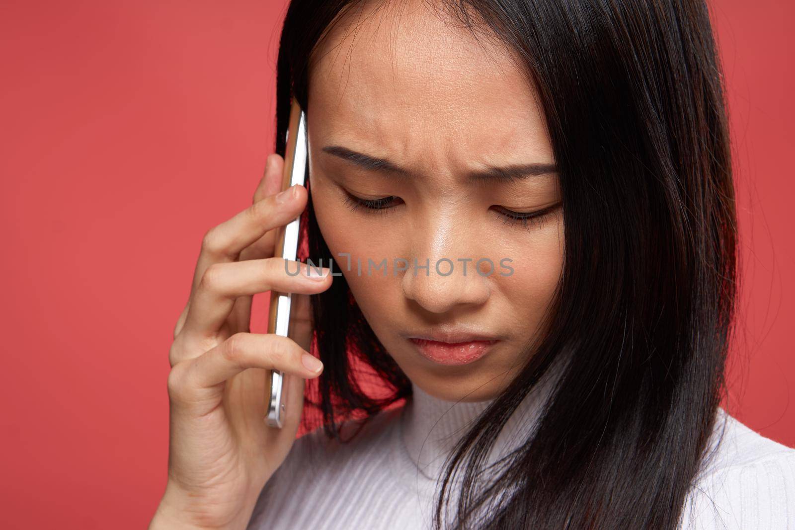 sad asian woman talking on the phone close-up red background by SHOTPRIME