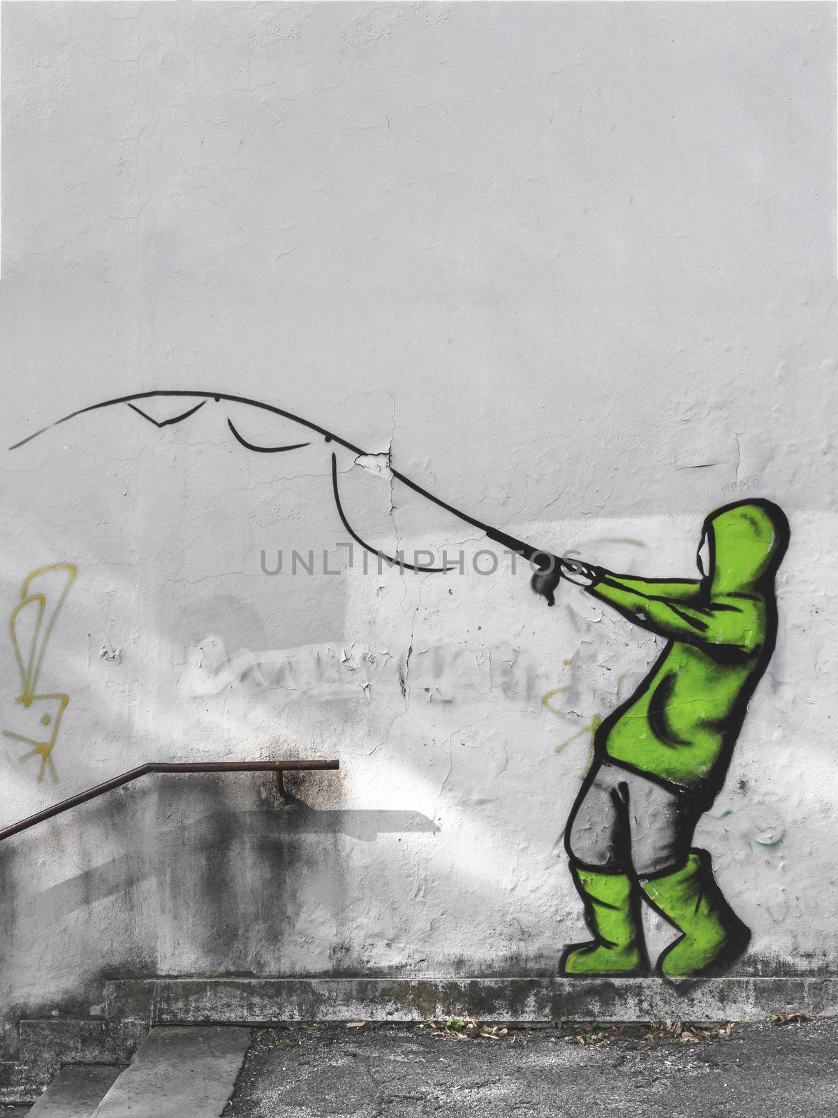 Street art by unknown artist on a concrete wall. The painting represents a boy fishing, suit with raincoat and green galoshes. Vertical copy space.