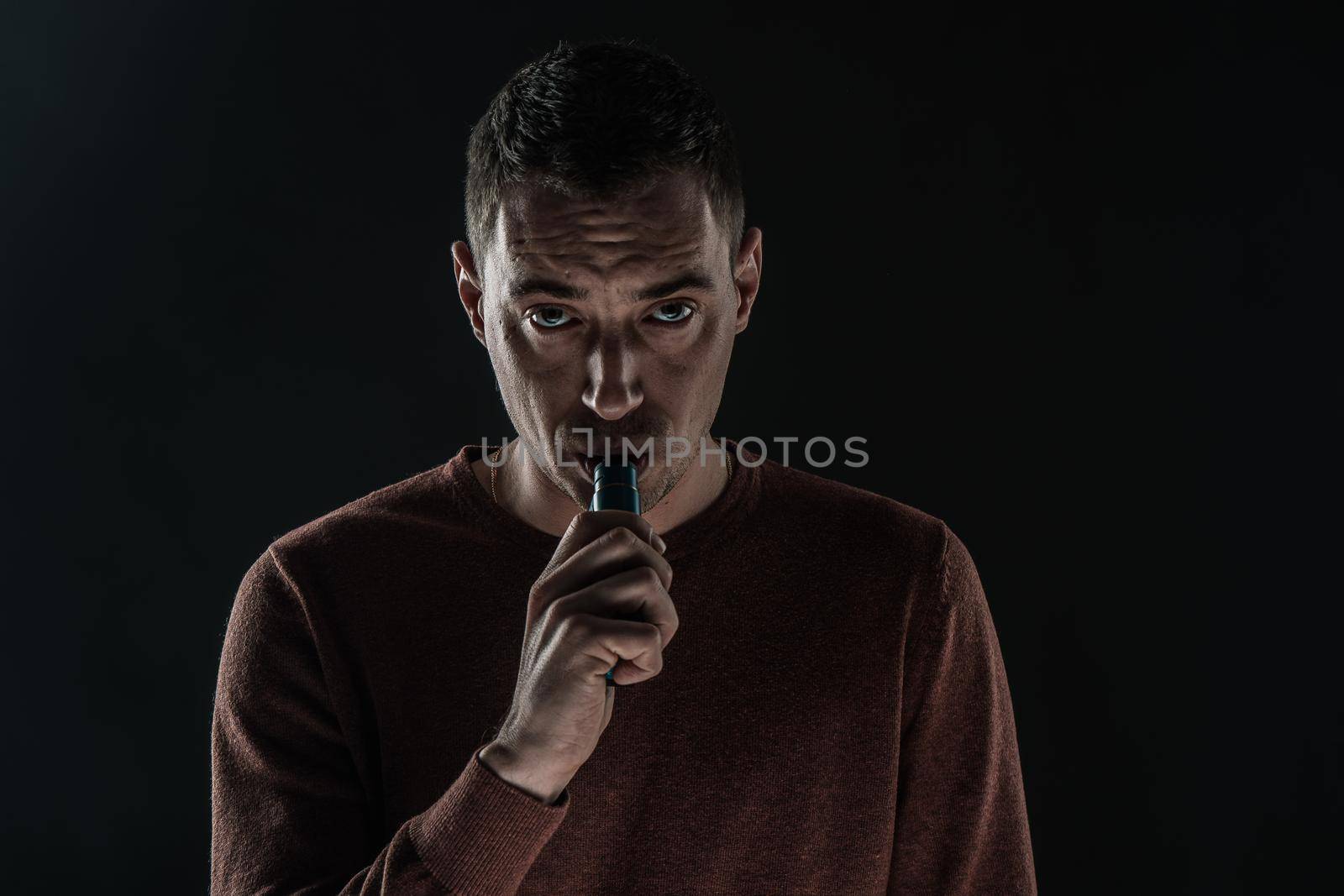 a man smokes a vape on a black background white smoke steam portrait close-up. High quality photo
