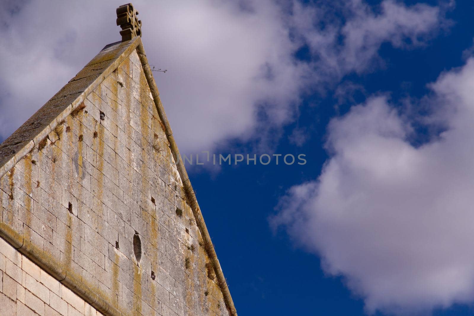 Close-up of a triangular stone wall with a cross on the top against a blue sky