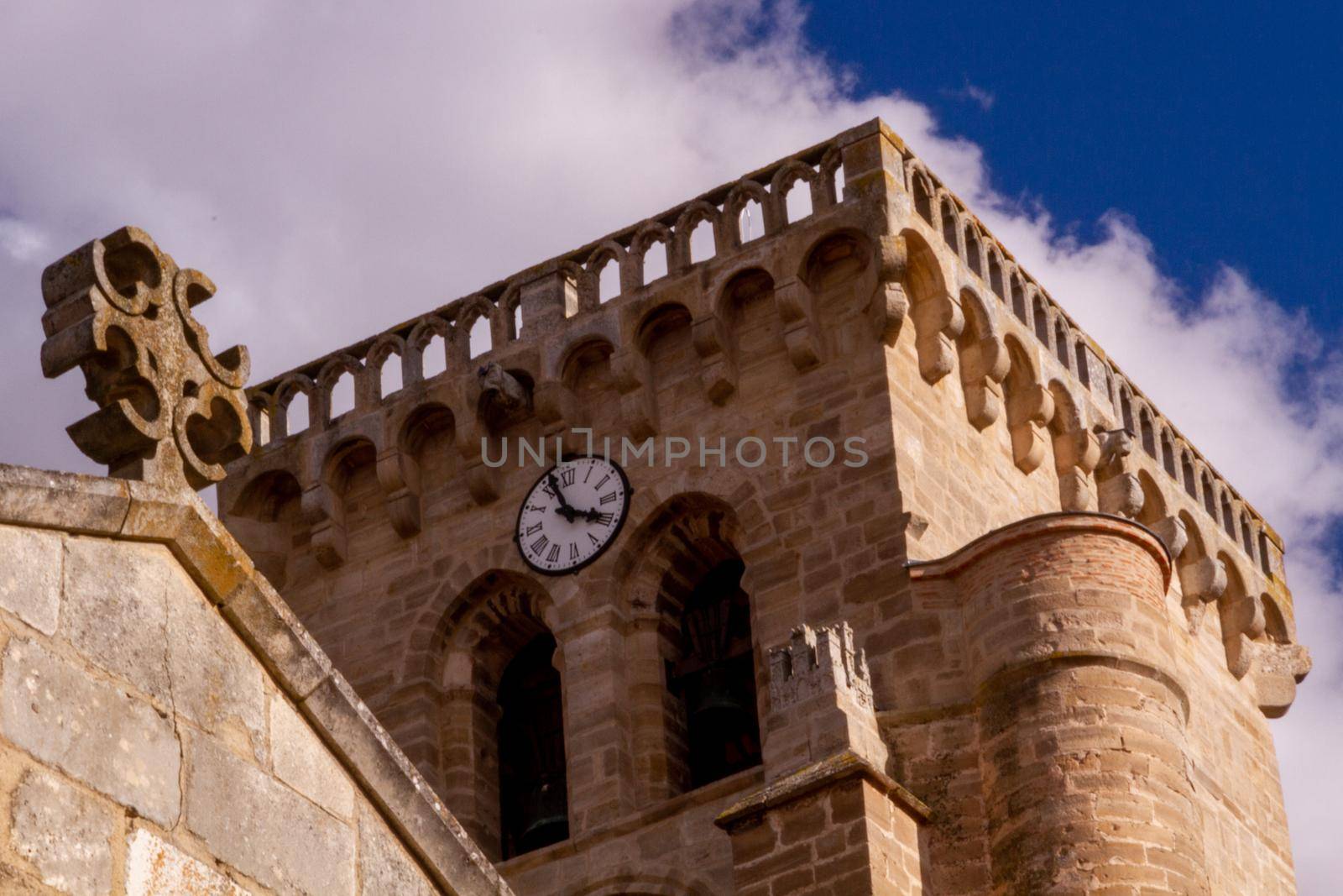 A cross on the top of a stone wall in front of a clock tower against a blue sky on a sunny day