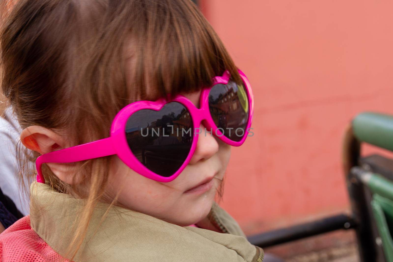 A cute, brown-haired baby girl wearing pink sunglasses and a green jacket