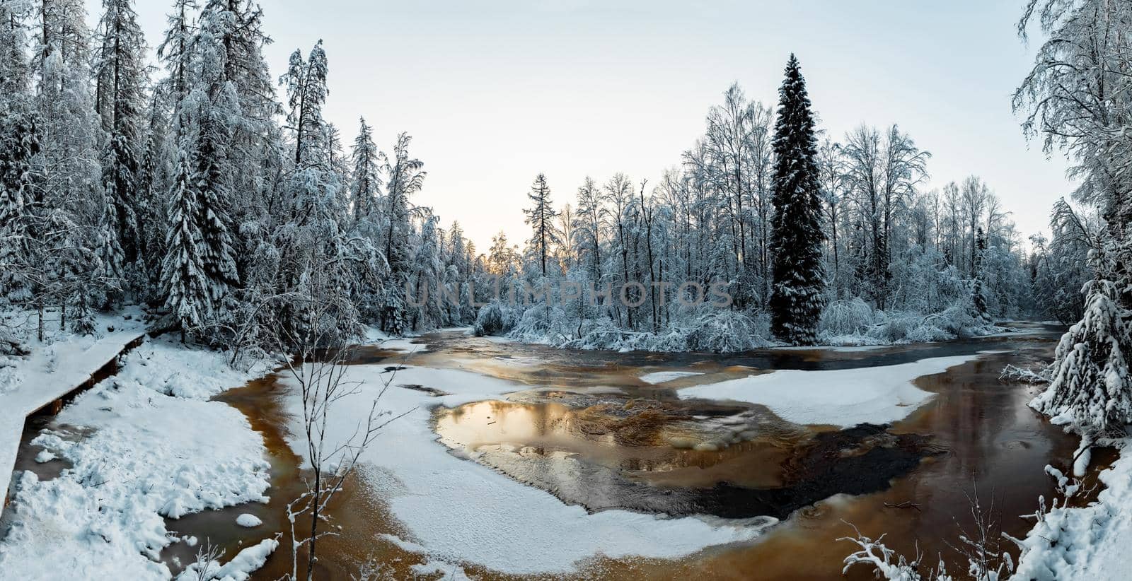 The wild nature at sunset, the wild frozen small river in the winter wood, the Red River, ice, snow-covered trees. High quality photo