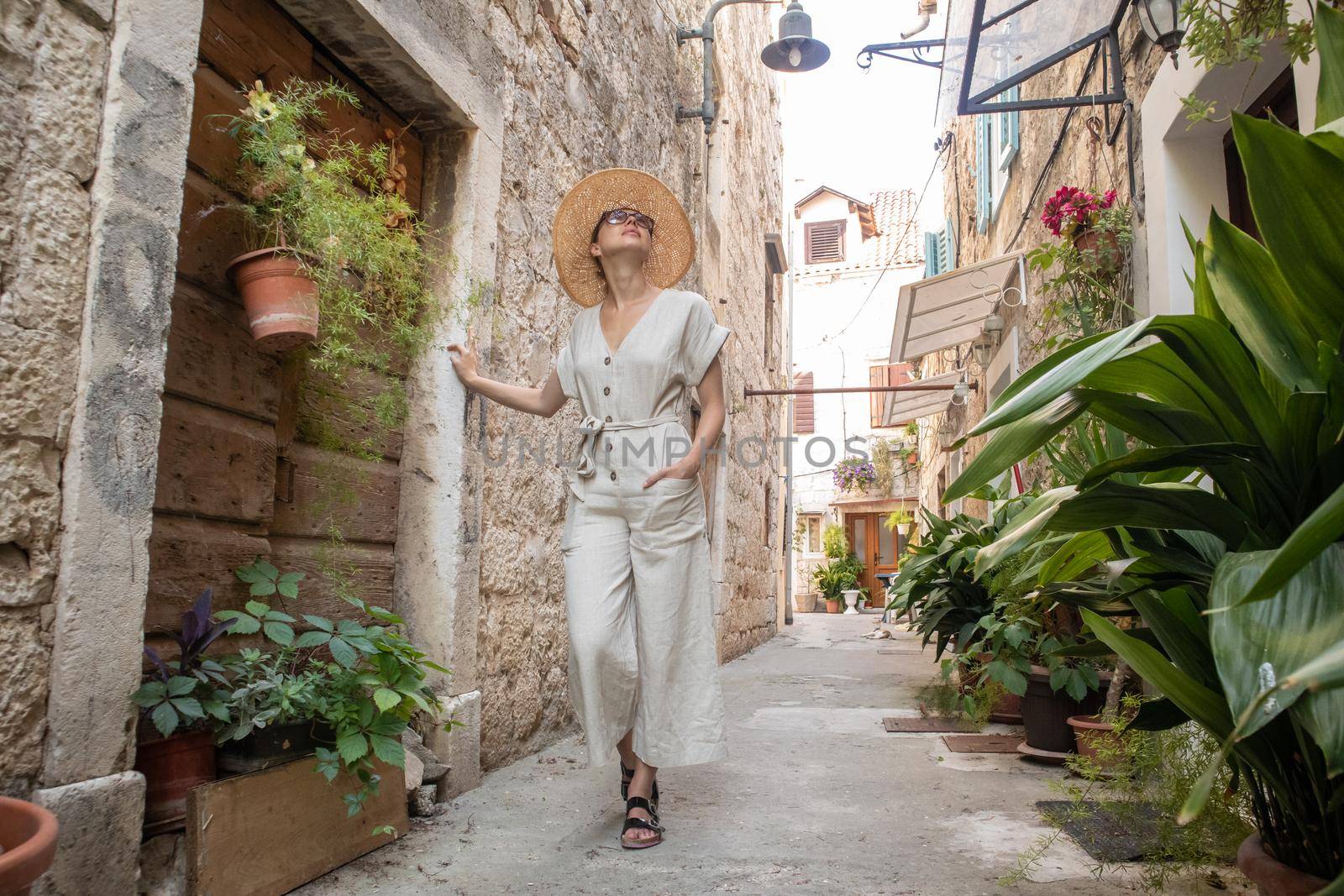 Beautiful blonde young female traveler wearing straw sun hat sightseeing and enjoying summer vacation in an old traditional costal town at Adriatic cost, Croatia