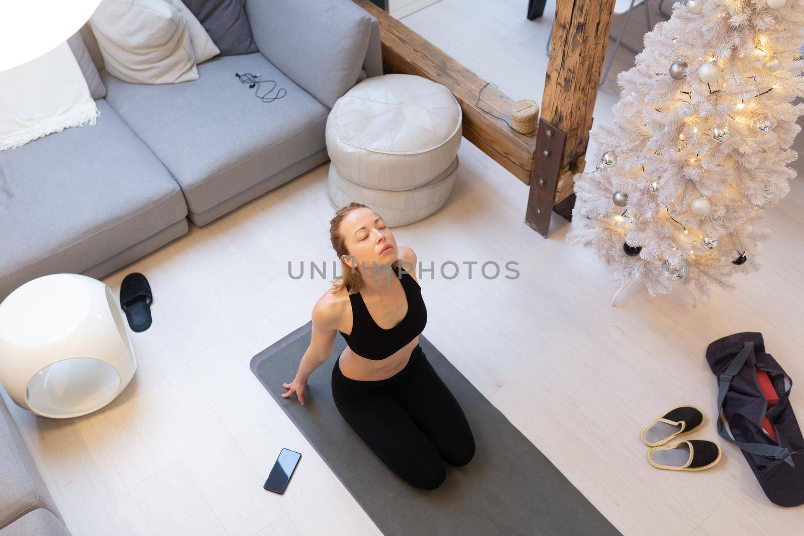 Beautiful blonde woman doing home workout indoors. Woman practice yoga at home. Fit girl using workout tutorials for healthy active lifestyle. Woman using quarantine for home workouts and stretching