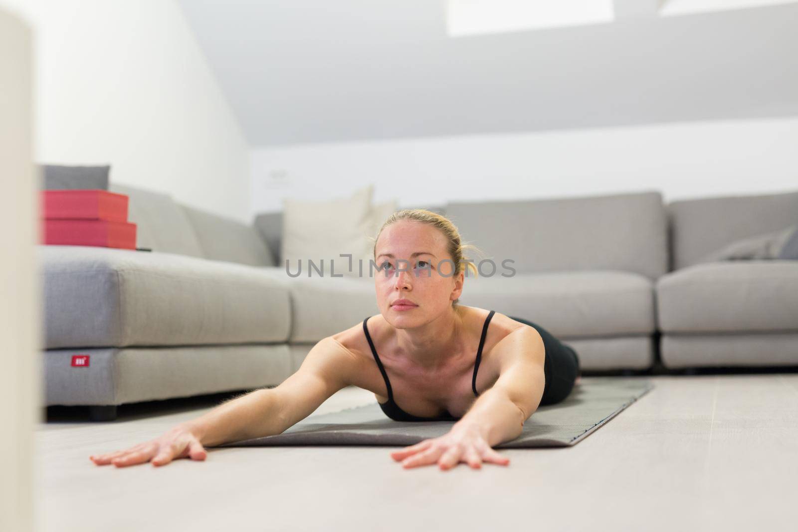 Beautiful blonde woman doing home workout indoors. Woman practice yoga at home. Fit girl using workout tutorials for healthy active lifestyle. Woman using quarantine for home workouts. Stretching