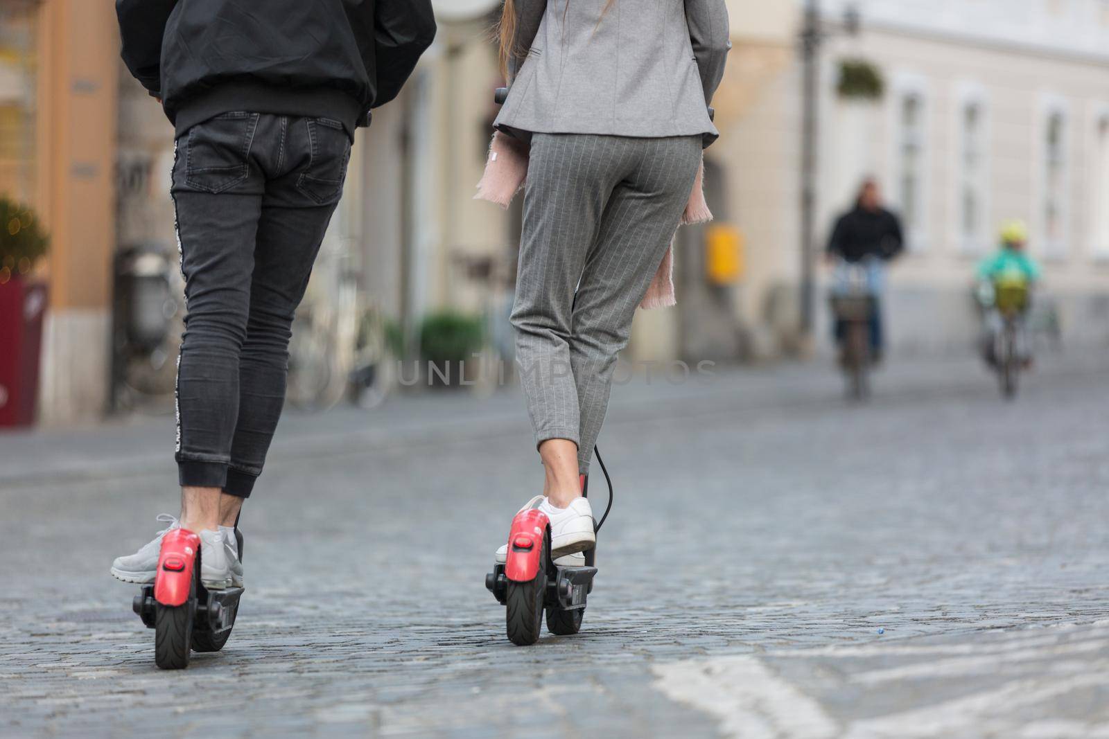 Rear view of unrecognizable trendy fashinable teenagers riding public rental electric scooters in urban city environment. New eco-friendly modern public city transport in Ljubljana, Slovenia.