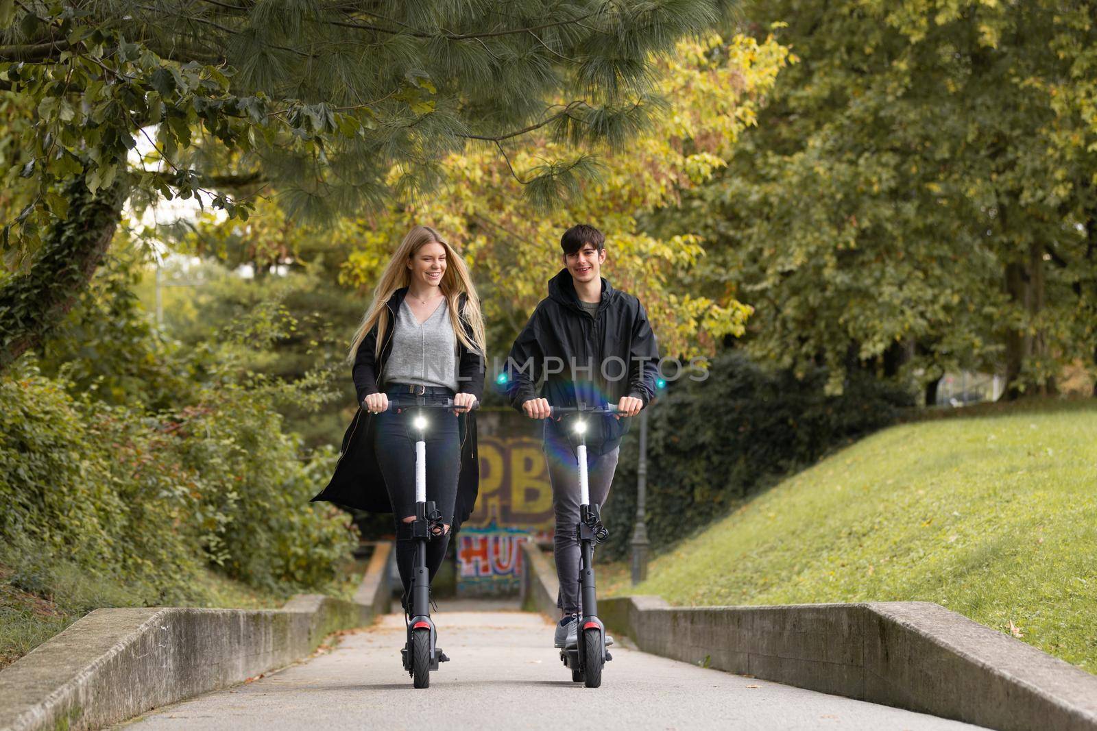 Trendy fashinable teenagers riding public rental electric scooters in urban city park. New eco-friendly modern public city transport in Ljubljana, Slovenia by kasto