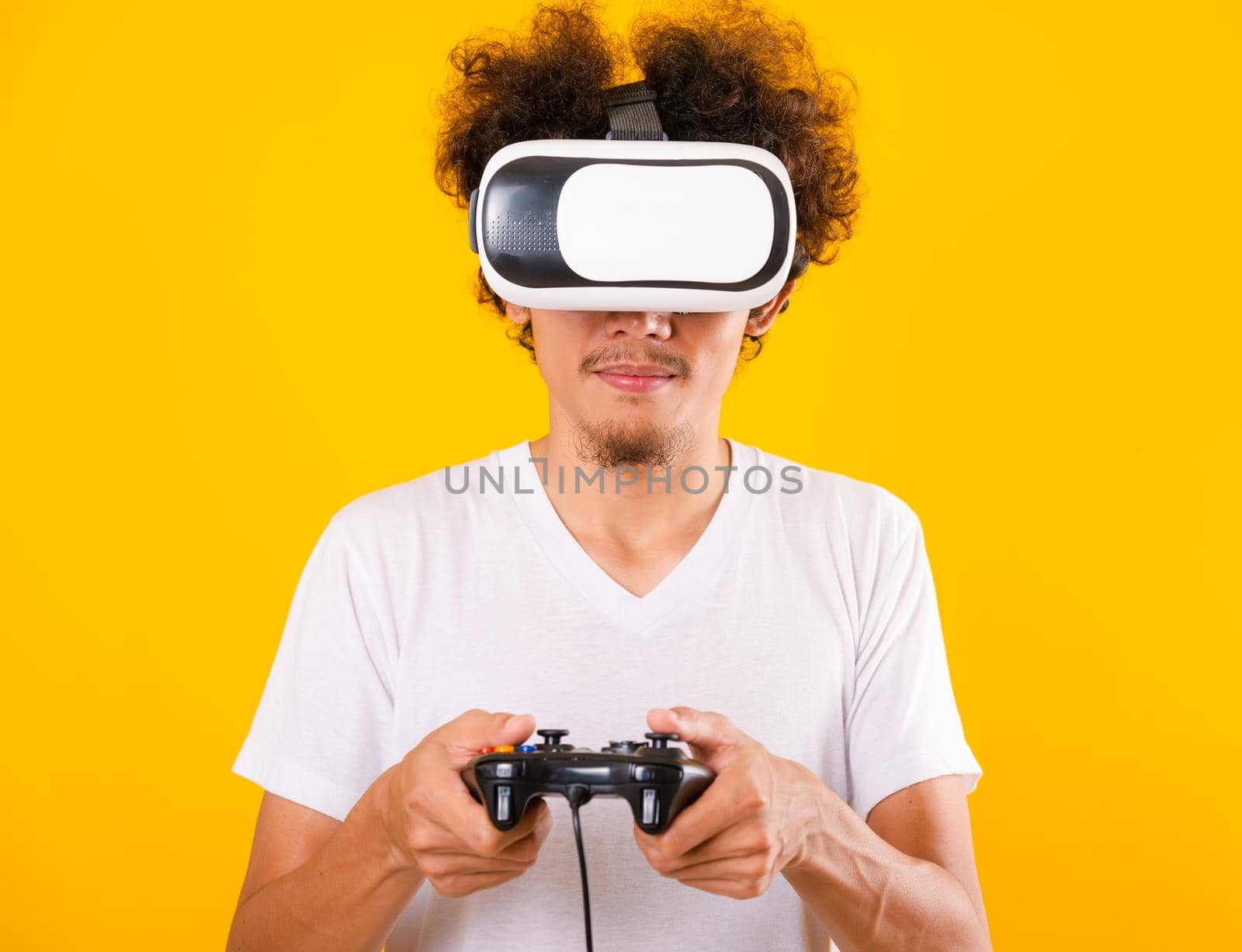 Asian handsome man with curly hair play game he using virtual reality headset or VR glass isolate on yellow background with copy space for text