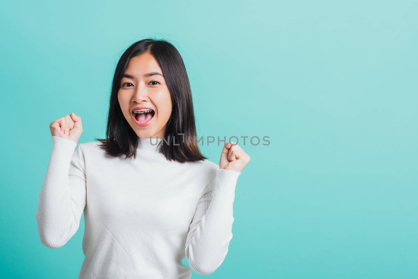 Young beautiful Asian woman cheerful surprised and amazed for success with arms raised, Portrait happy female glad-hands arms fists raised great big win competition, isolated on a blue background