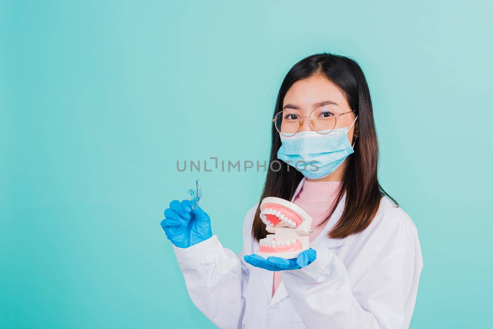 Asian beautiful woman dentist holding silicone orthodontic retainers and model teeth denture isolated on blue background, Teeth retaining tools after removable braces, Orthodontics dental healthy care