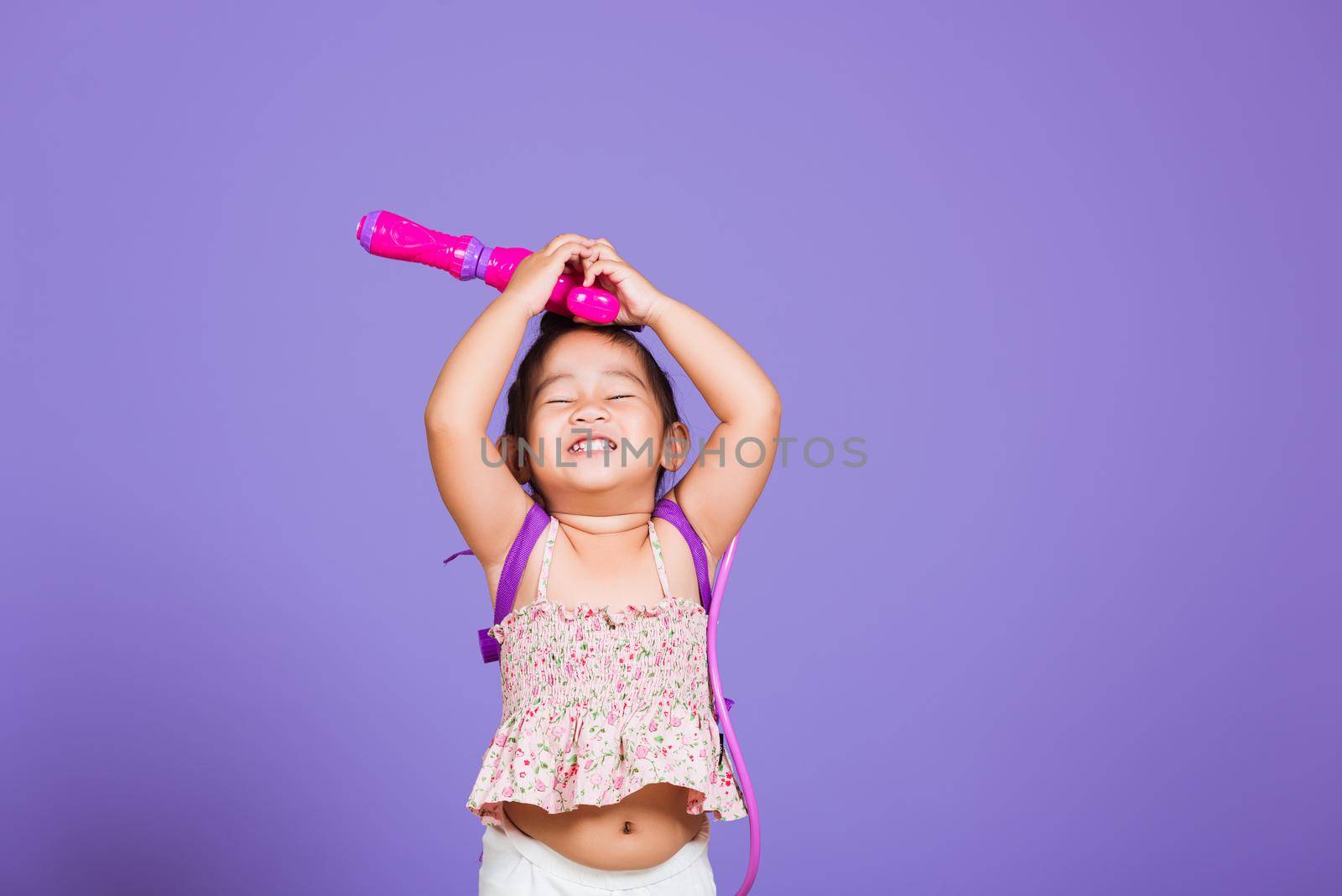Thai child funny hold toy water pistol and smile, Happy Asian little girl holding plastic water gun, studio shot isolated on purple background, Thailand Songkran festival day national culture concept