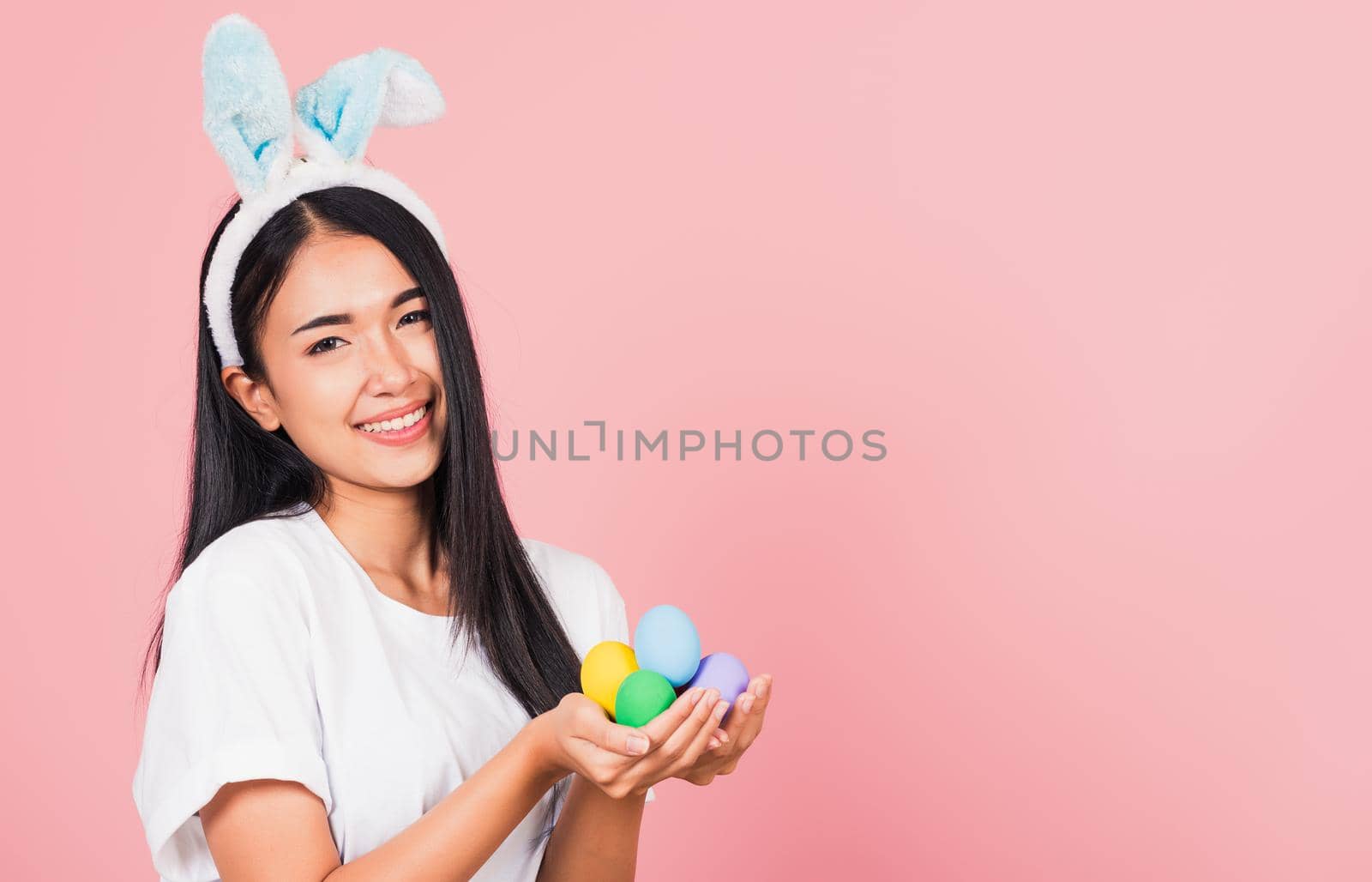 Happy Easter concept. Beautiful young woman smiling wearing rabbit ears holding colorful Easter eggs gift on hands, Portrait female looking at camera, studio shot isolated on pink background