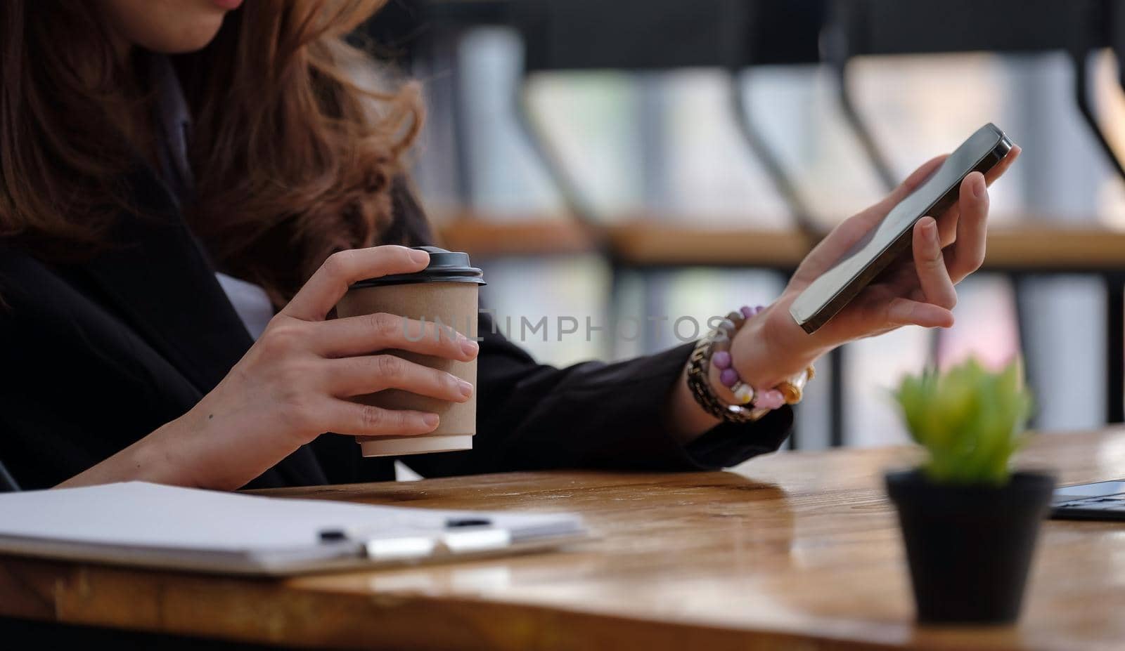 Young Asian woman with smartphone while holding cup of coffee and texting text message on smartphone app