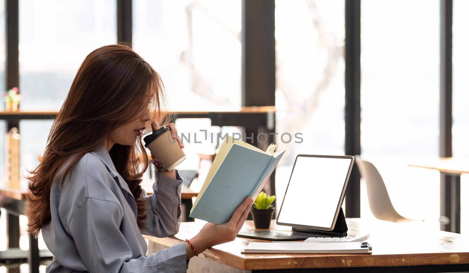 Asian woman working with tablet while reading data on notebook. Student girl working at home. Work or study from home, freelance, business, lifestyle concept. by nateemee