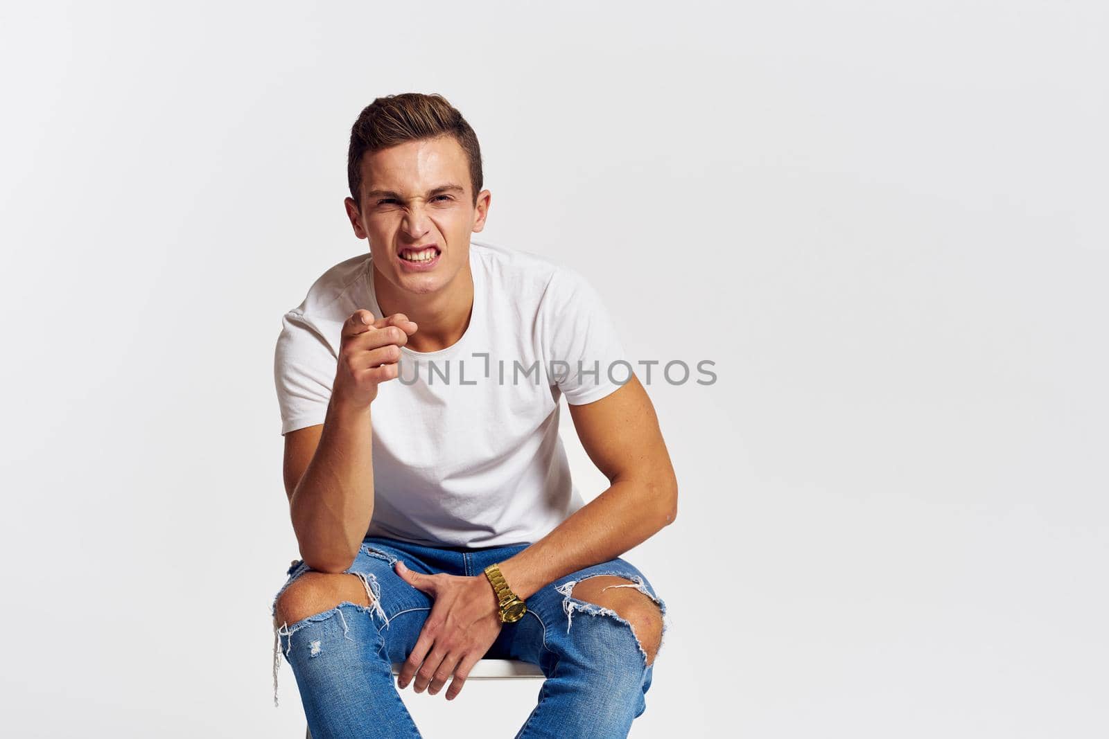 Man on a chair indoors torn jeans white t-shirt handsome face model light background. High quality photo