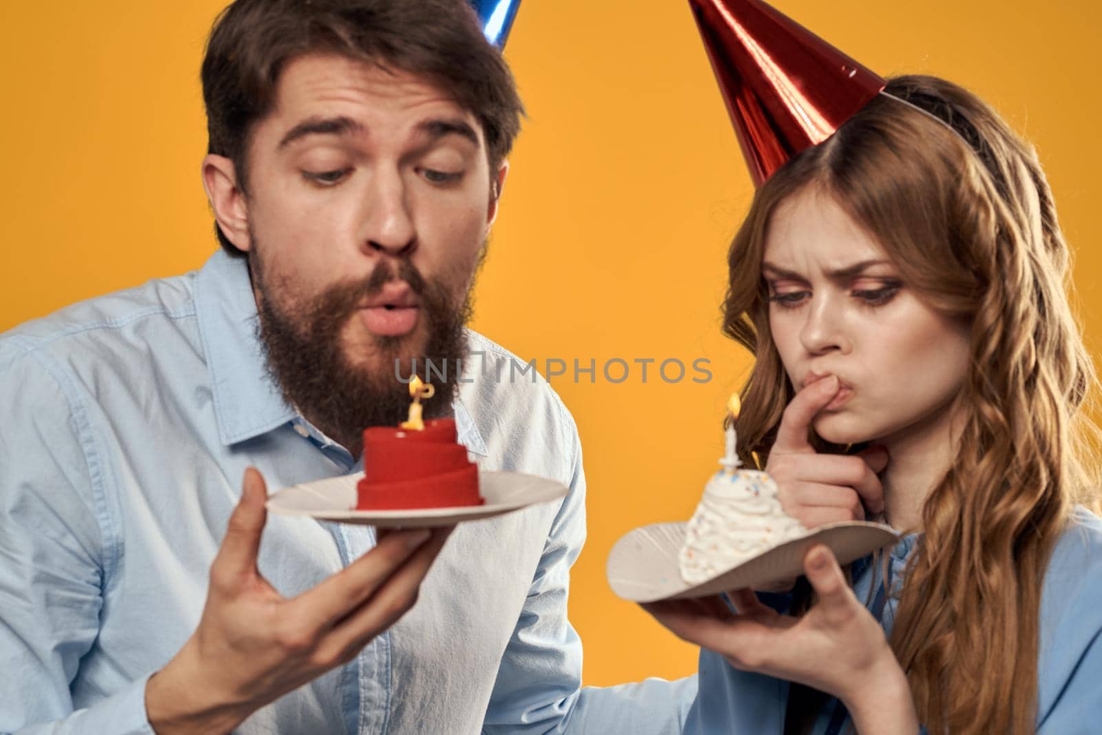 Birthday party man and woman on a yellow background in hats with a cake in their hands. High quality photo