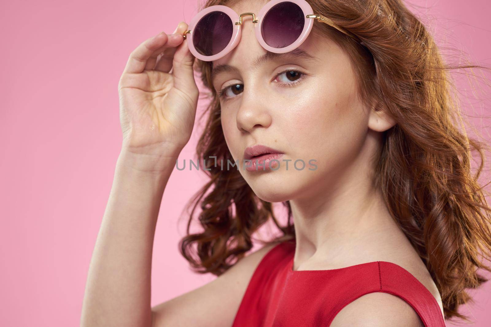 Girl with curly hair dark round glasses fun red dress pink background. High quality photo