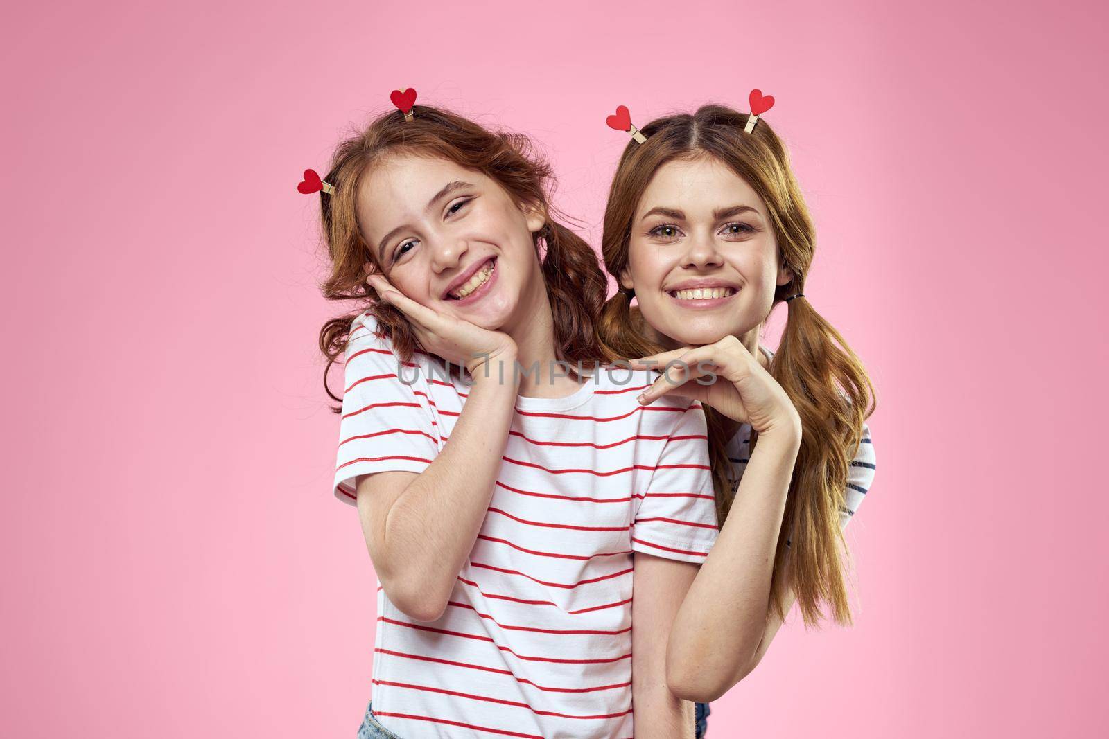 Happy sisters are having fun on a pink background and heart-shaped clothespins on their heads. High quality photo