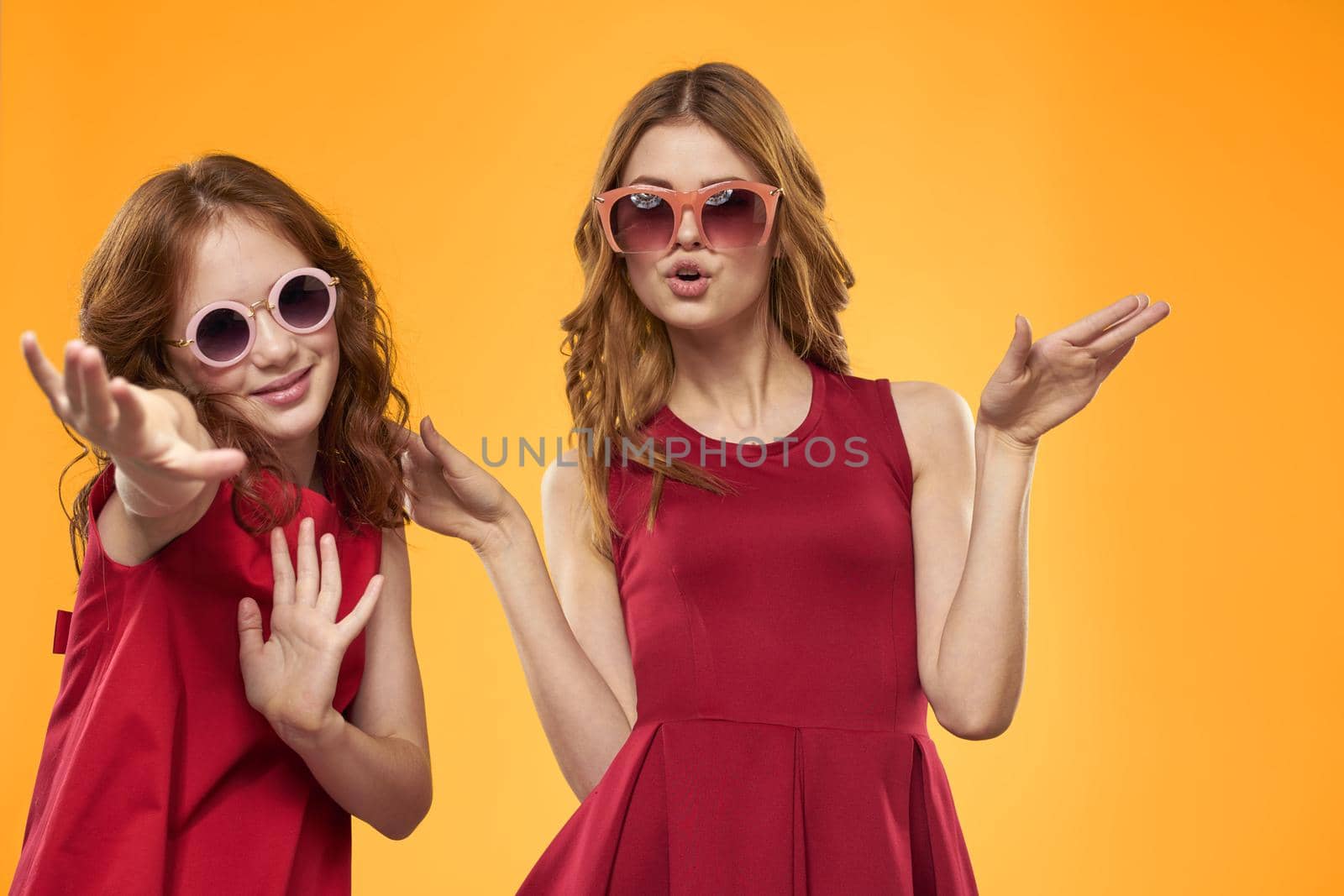cheerful mom and daughter wearing sunglasses lifestyle friendship family yellow background studio. High quality photo