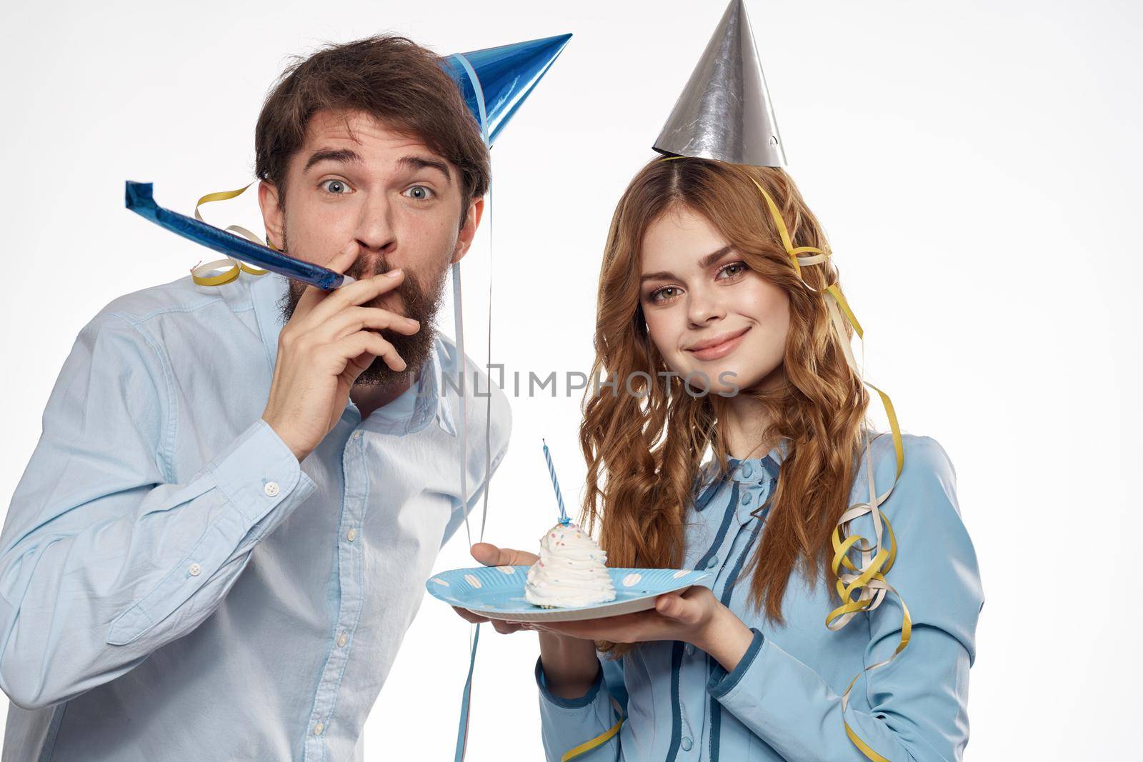 energetic man and woman with a cake and in hats celebrate a birthday on a light background. High quality photo