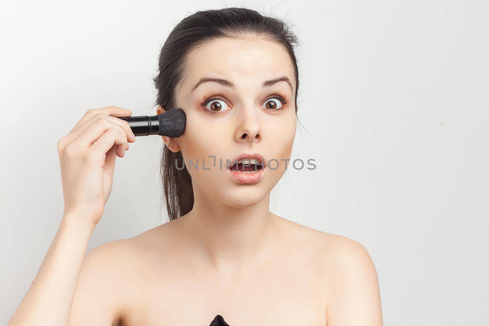 woman with bare shoulders applying makeup brush on face. High quality photo