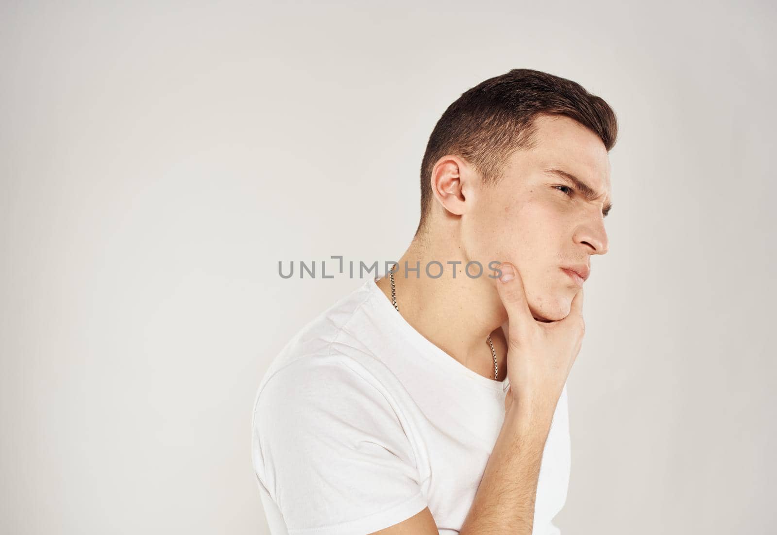 A man on a light background touches his face with his hand and a white T-shirt model by SHOTPRIME