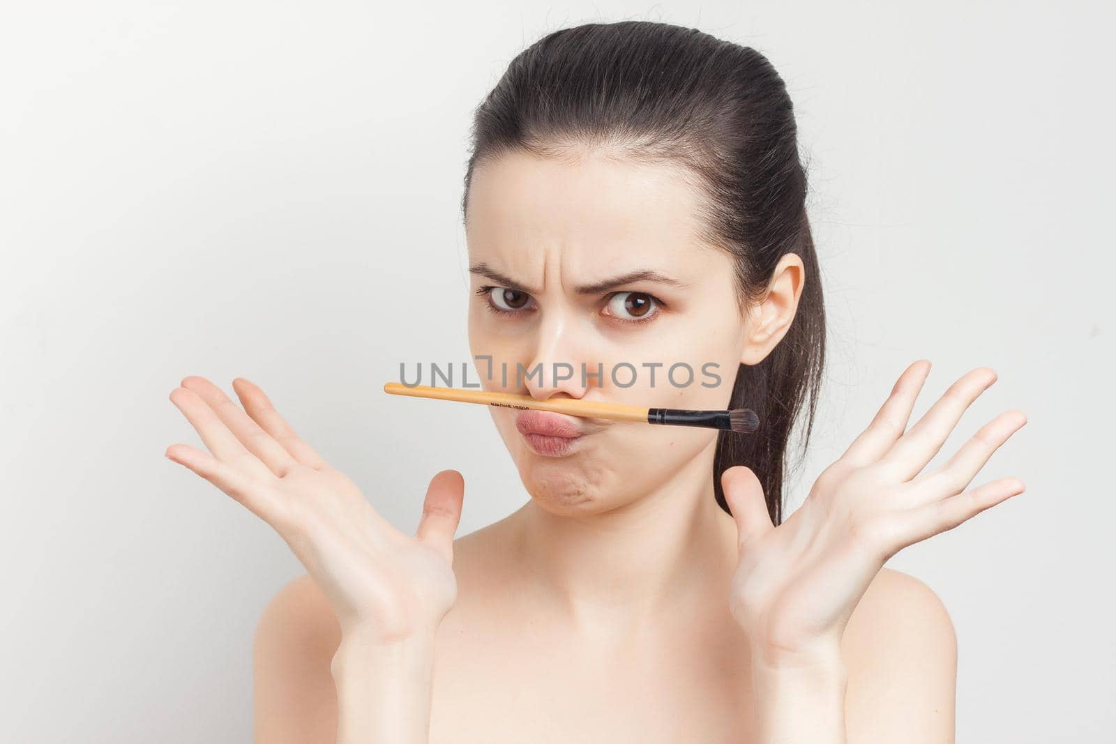 brunette holding makeup brush skin care face cream bare shoulders. High quality photo