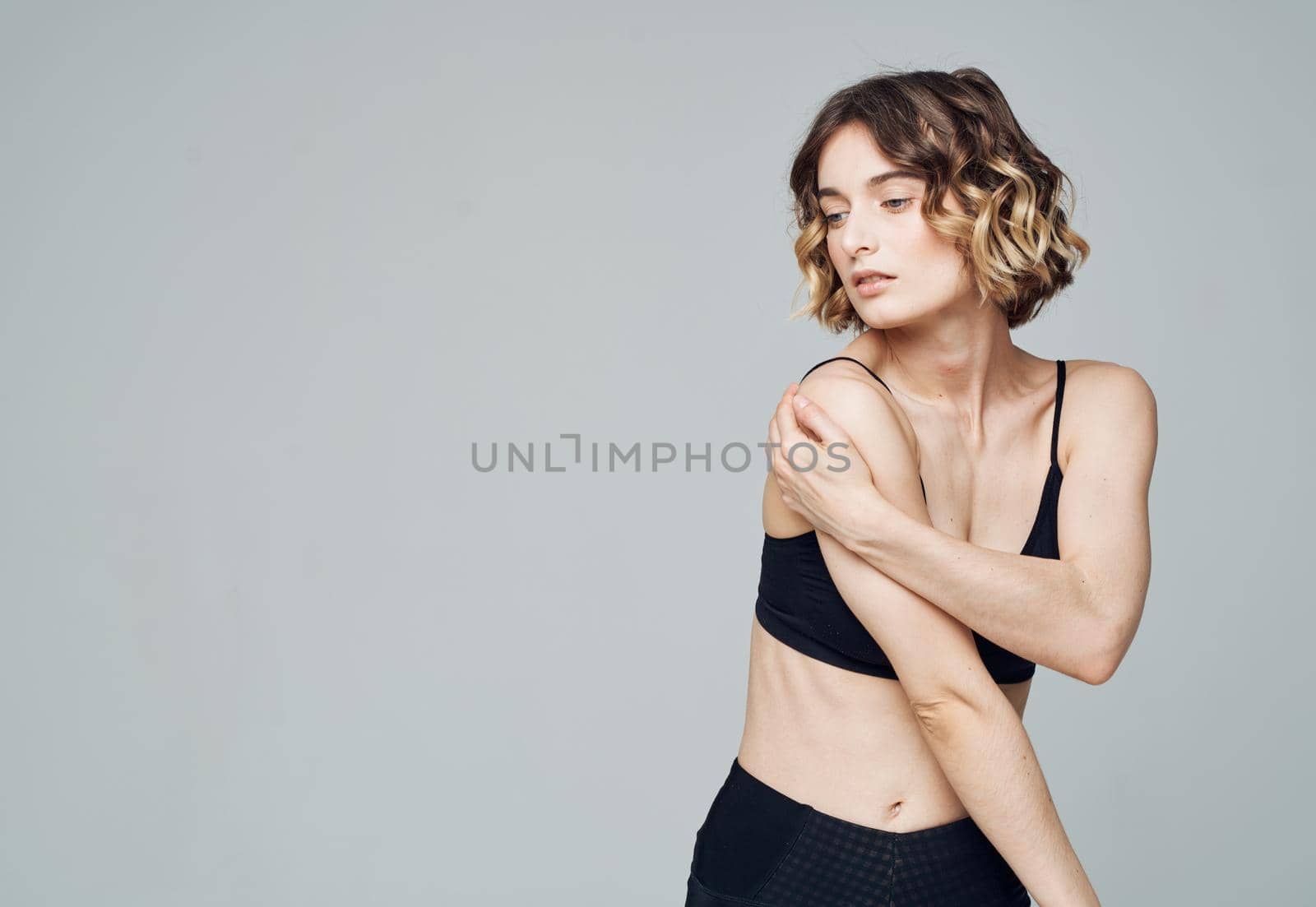 slender woman in sportswear touches herself with hands on a gray background. High quality photo
