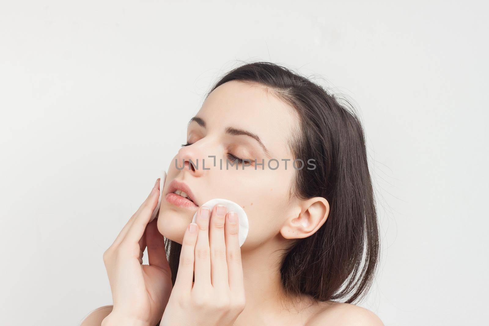 brunette naked shoulders wipes her face but clean skin with a sponge. High quality photo