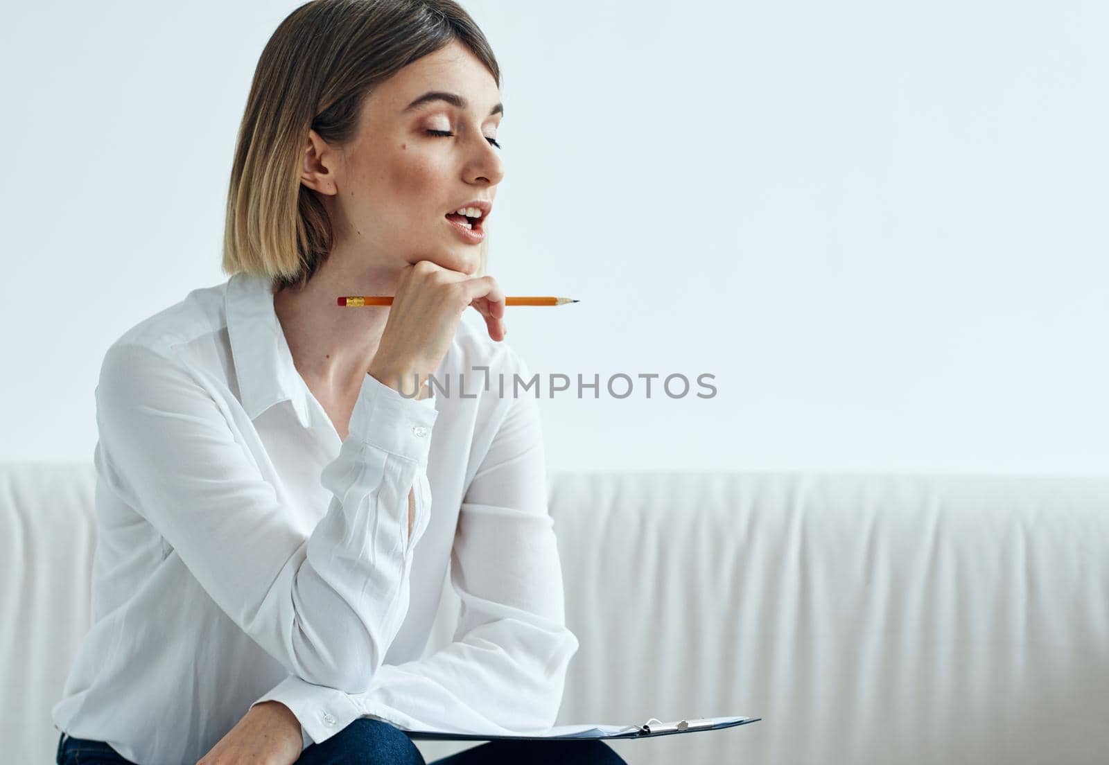 A woman sits on a sofa In a bright room in a shirt and papers on her lap. High quality photo