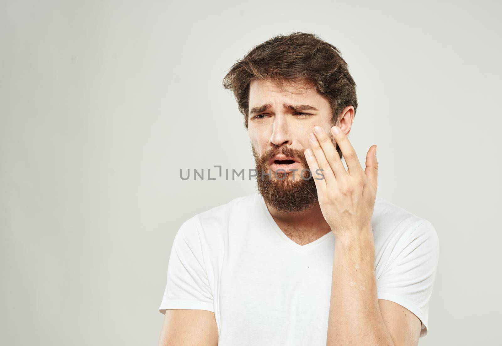 Nice guy with a beard in a white T-shirt on a light background cropped view of a sad face. High quality photo