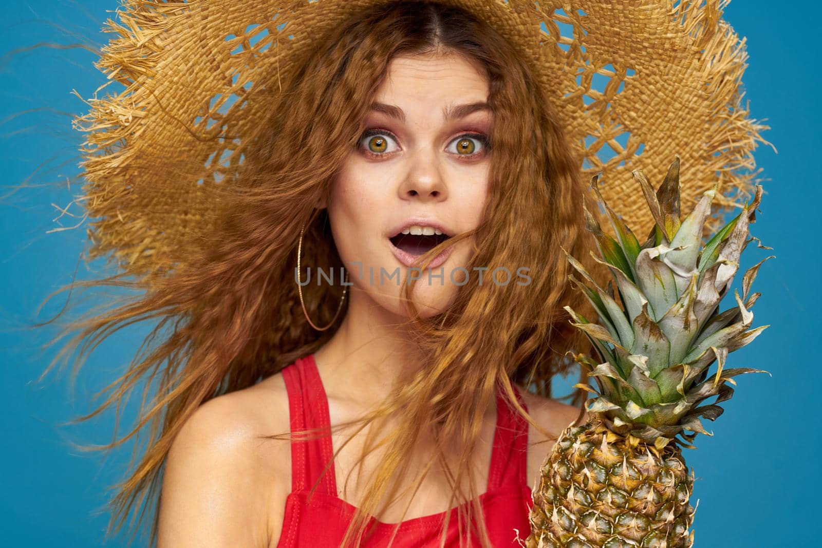 Woman in a straw hat with pineapple in her hands wavy hair exotic fruits you summer blue background vacation by SHOTPRIME