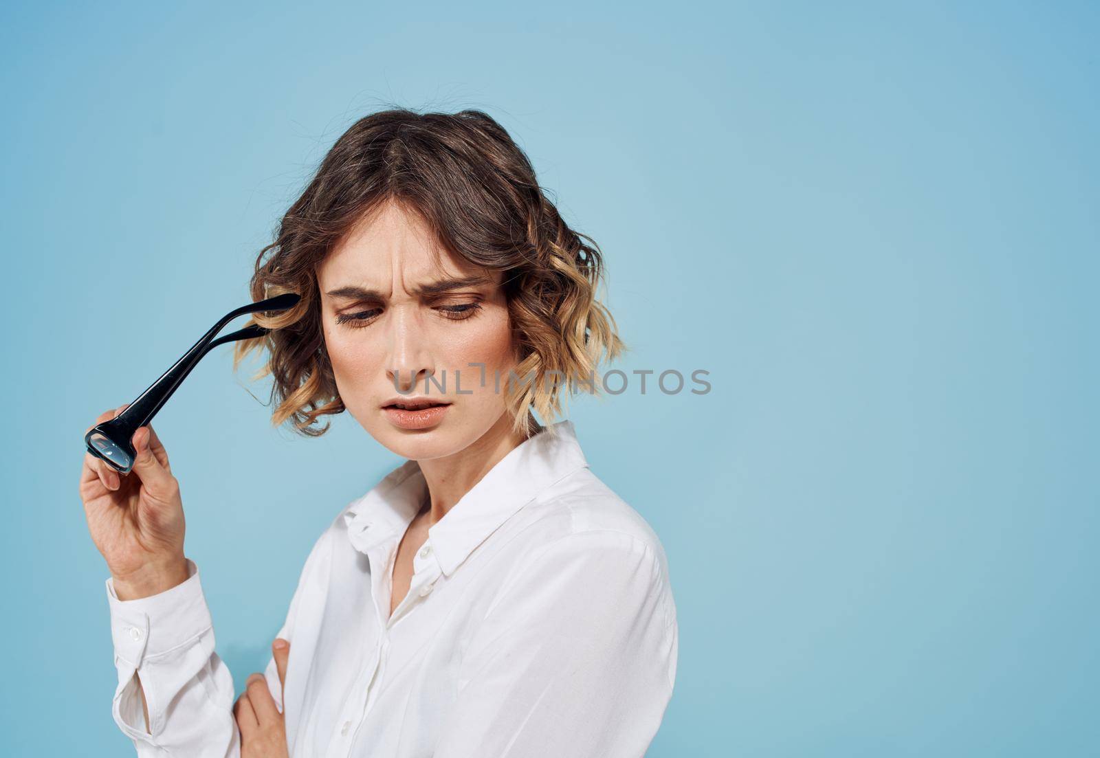 Fashionable woman in a light shirt with glasses in her hands on a blue background. High quality photo