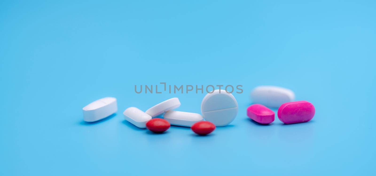 Pharmacy banner. White and pink tablets pills on blue background. Round and oval tablets. Painkiller medicine. Acetaminophen and ibuprofen tablets pills. Pharmaceutical industry. Painkiller tablets. by Fahroni