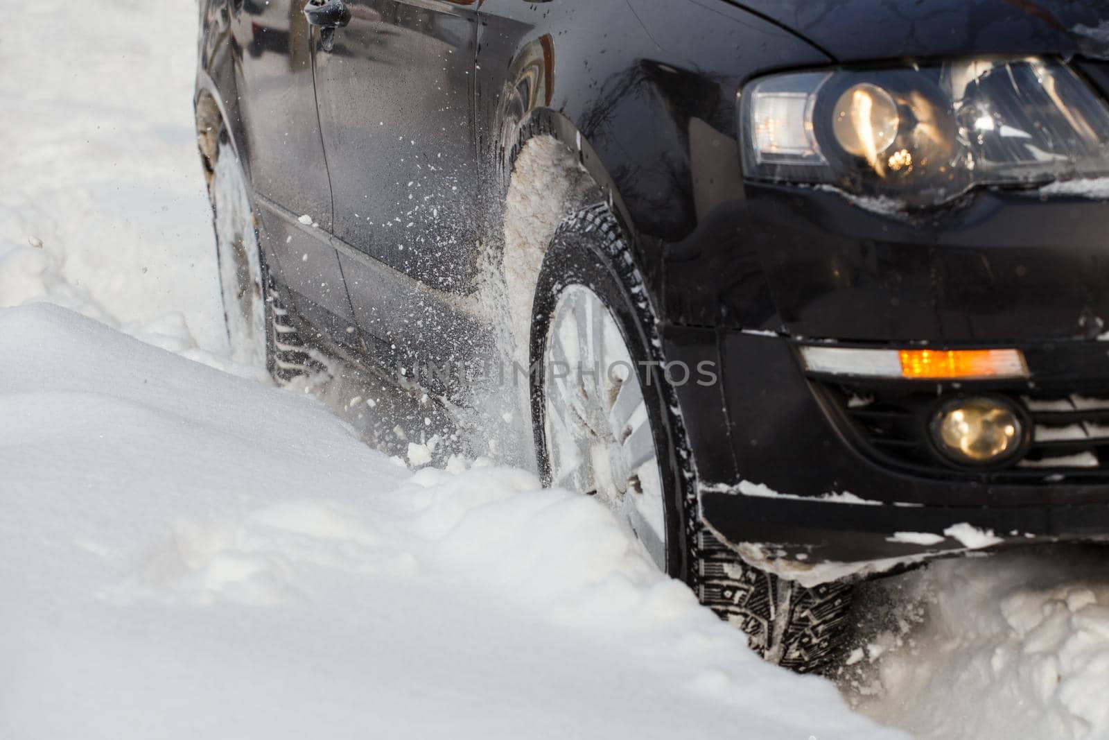 Black vehicle makes its way through the deep snow rut skidding, car's wheels spin and spew up pieces of snow it attempts to gain traction on the slippery road.