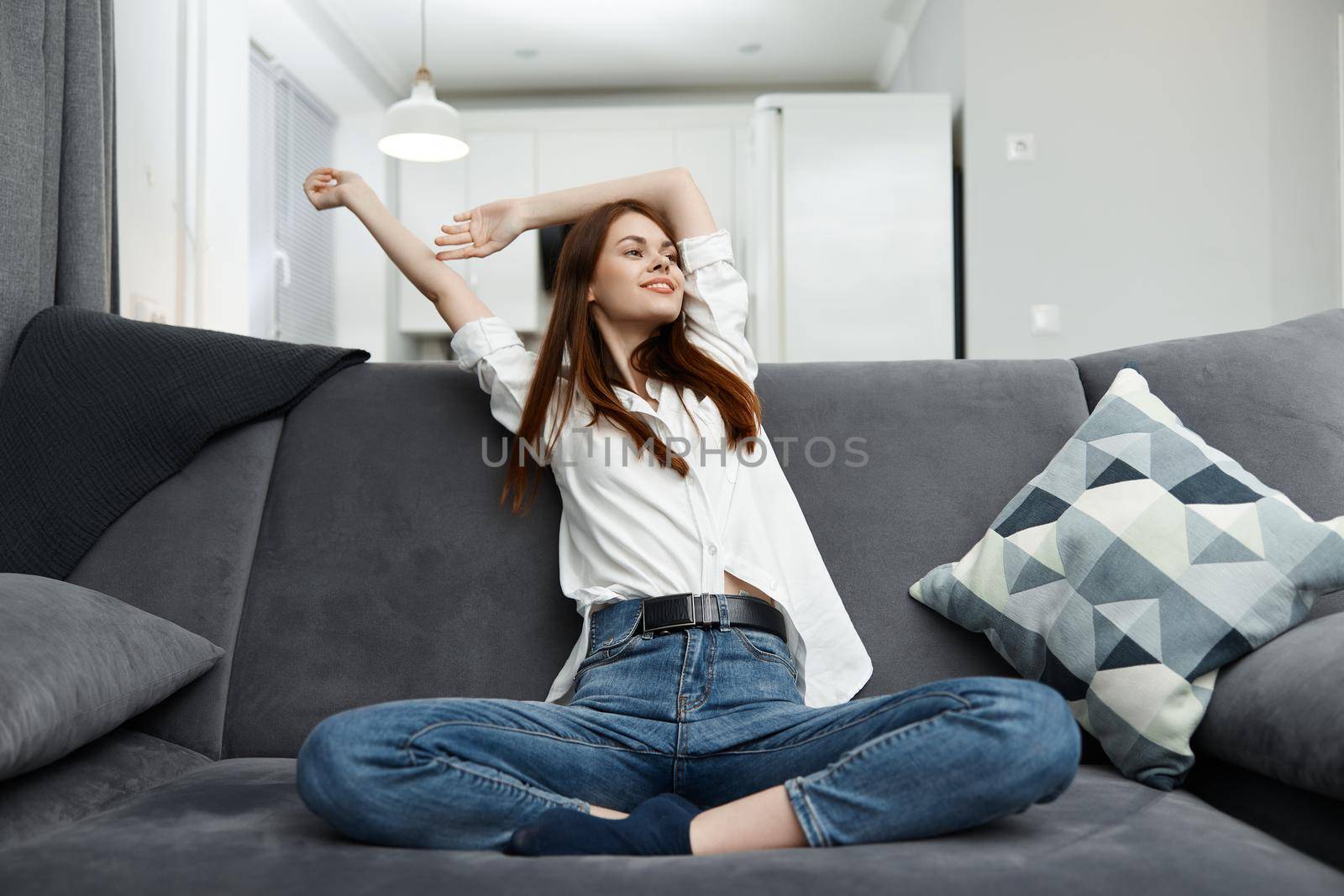 cheerful woman holding her hands behind her head relaxing on the couch in the apartment. High quality photo