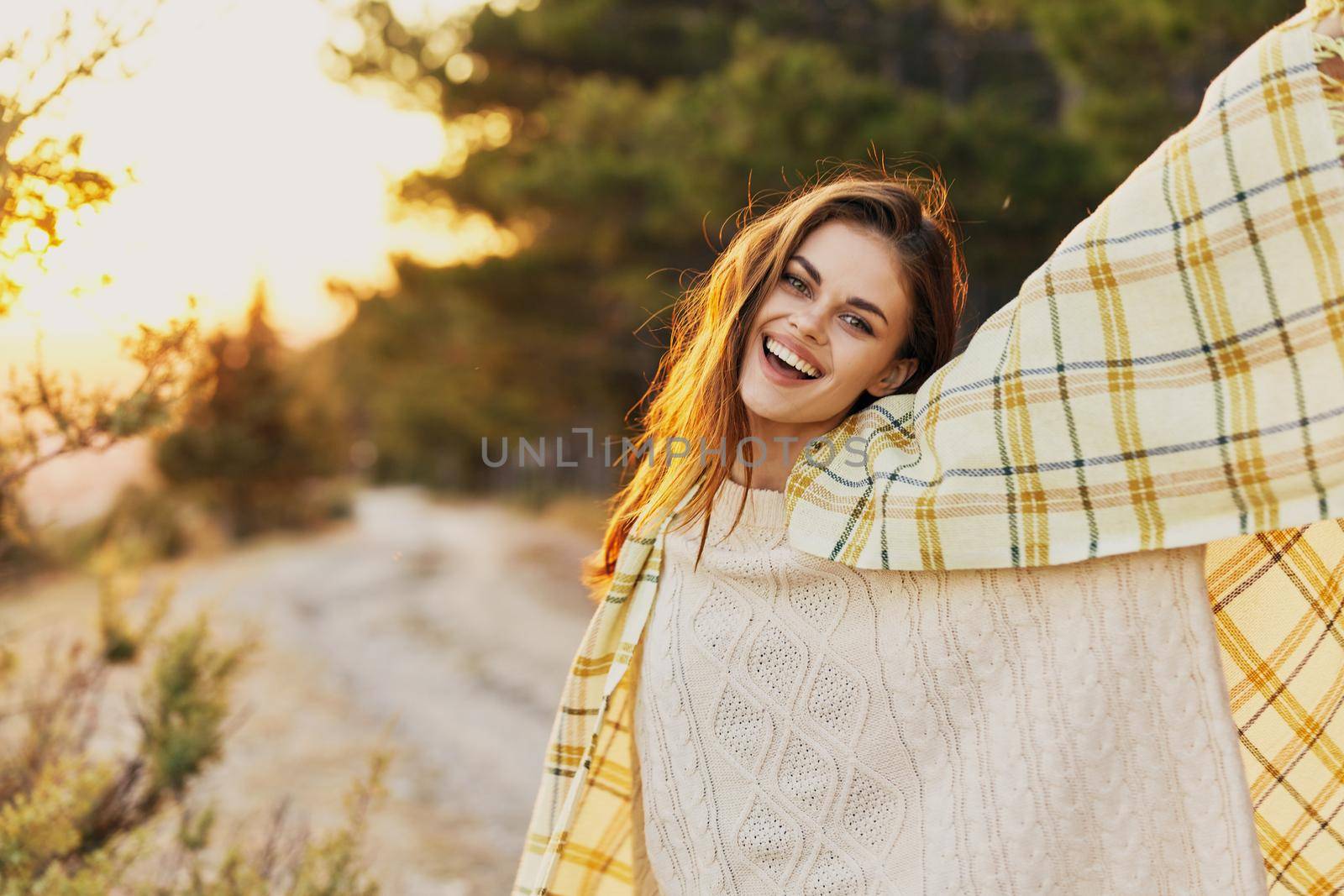 Happy woman near the coniferous forest with a blanket on her shoulders at sunset. High quality photo