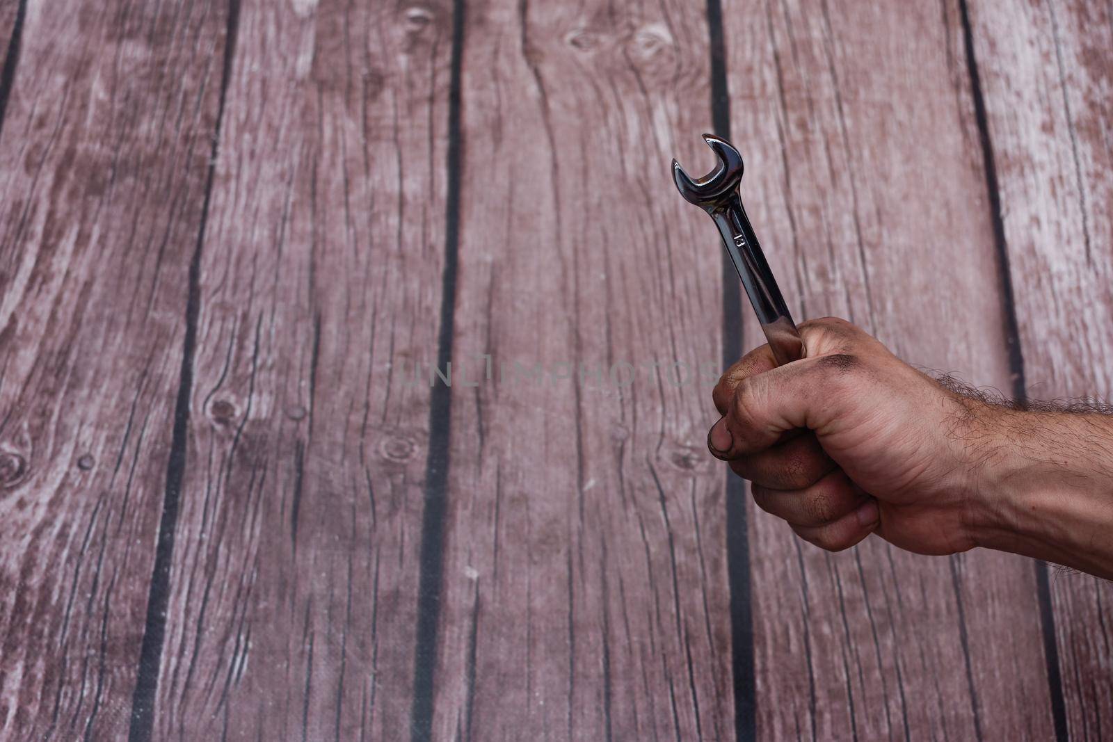 Wrench in hand. the oily, dirty working hands are clenched into a fist with a spanner. On a wooden background. copy space